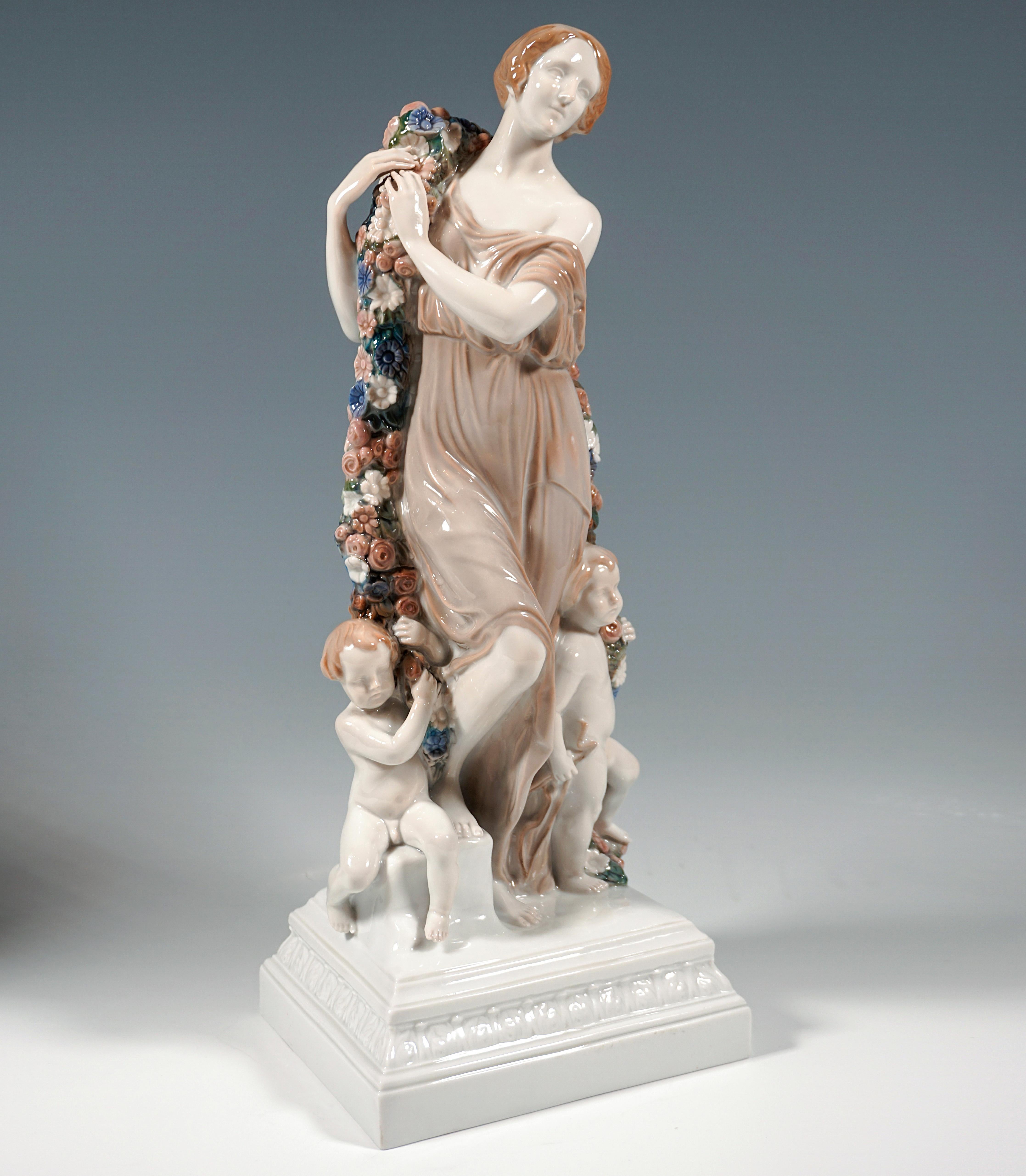 Extremely Rare Large Art Nouveau Group:
Monumental figure of Flora with chin-length hair in a long dress loosely embracing the beautiful body, her right foot resting on a low pedestal and holding with both hands a large, heavy garland of flowers