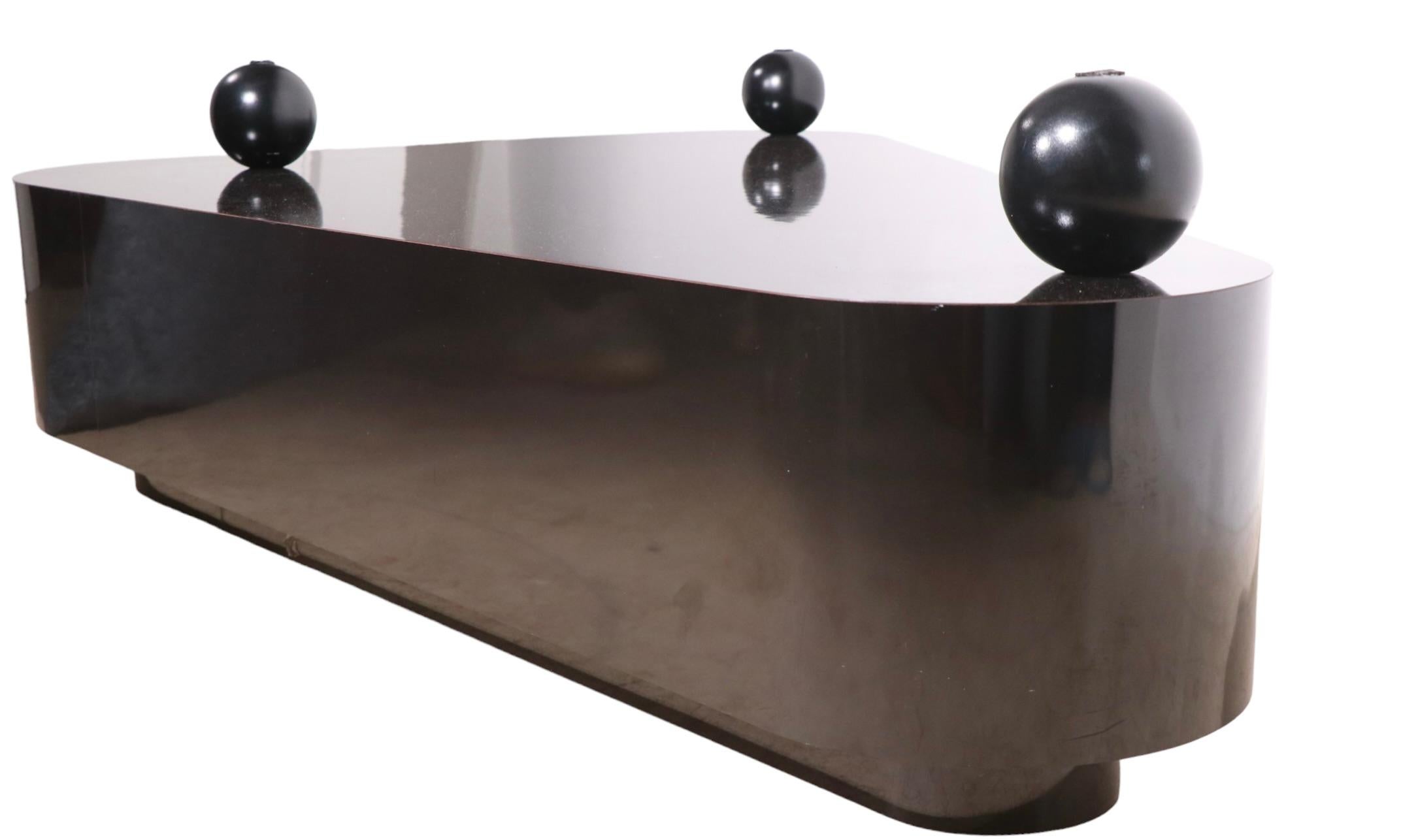 Spectacular two tier triangular coffee table, having a glossy black Formica base, with a thick ( 1 in. ) deeply textured plate glass top. The base features three balls, on which the glass top rests, and a hidden drawer. The glass top has a cool