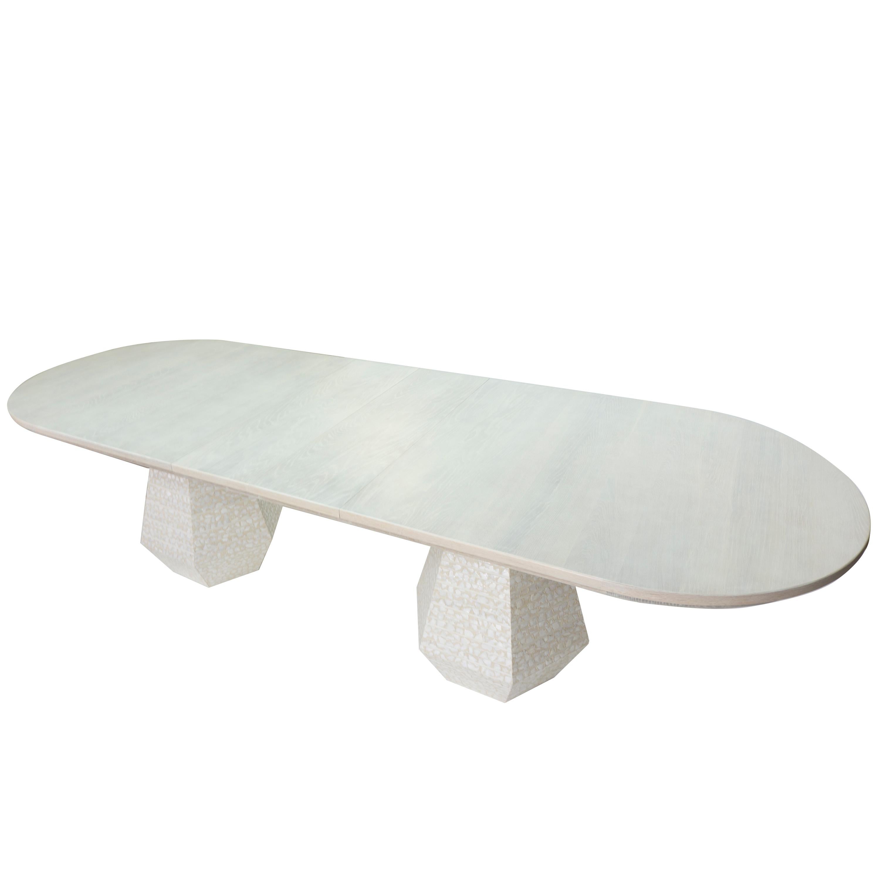 Our Capriz dining table is a postmodern design that is both minimal and spacious. The table features 2 hexagonal bases wrapped in a mother of pearl finish. The white oak top is lightly finished in cotton white and includes two extension leaves for a