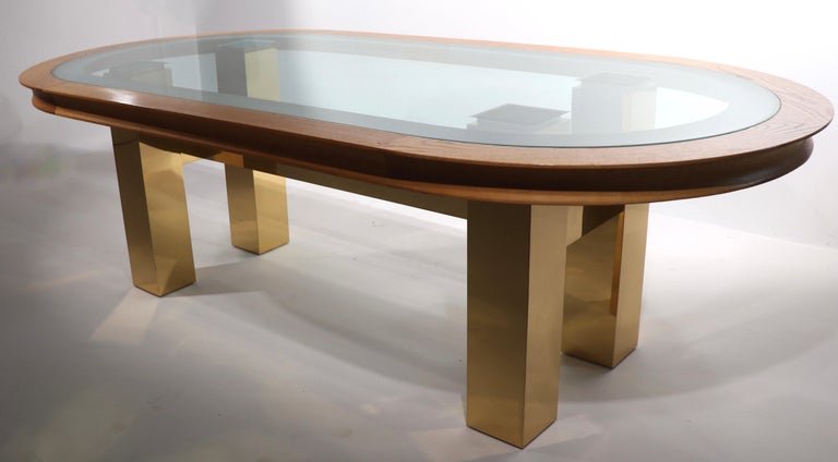 Spectacular oval dining table on Cityscape like architectural brass base, with inset oval glass top, on solid oak racetrack molding. Impressive scale, top quality design and construction, fine, original, clean and ready to use condition. Original