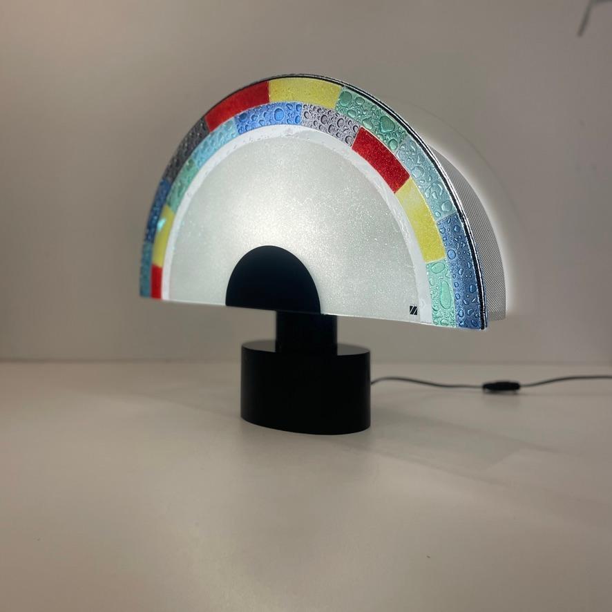 Large Post-Modern Table Lamp By Zonca.
The design of this lamp is a typical example of the 1980's post-modern style.
The Murano glass fan shape glass has the pastel colors of that period, not to forget the metal and resin black base, this color was