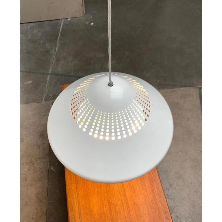 Lampada a sospensione danese con una suggestiva perforazione.

un design minimalista di dimensioni impressionanti. L'ombrello presenta una semplice forma a cono con curve morbide. L'ampia superficie del cono è interrotta da una perforazione