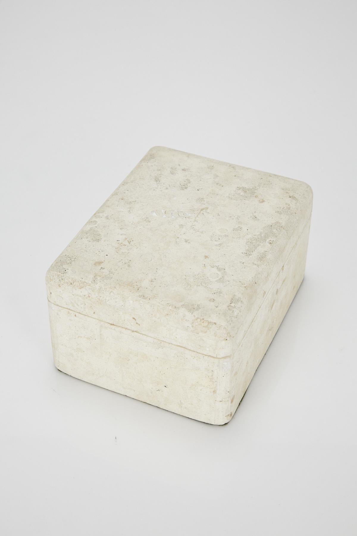 Large lidded box in matte white tessellated Mactan stone exterior and black felt-lined interior. Brass chain connects top and bottom. Underside lined in black felt. Simple rectangular form with lightly curved edges.

All furnishings are made from