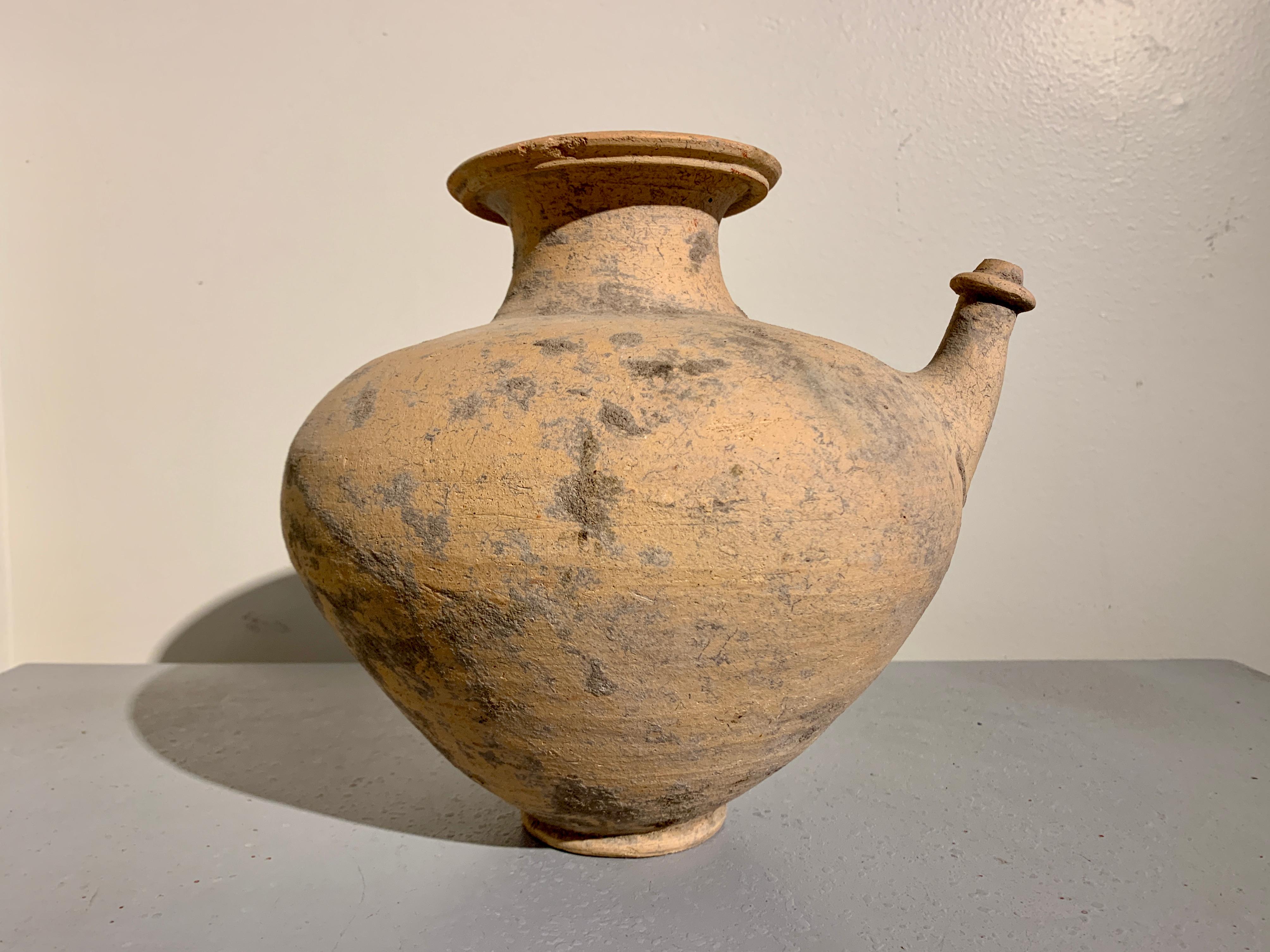 A very large ancient spouted pottery vessel, known as a kendi, Mon Dvaravati kingdom, circa 6th - 10th century, central Thailand.

Resting on a short, narrow ring foot, the large pottery vessel features a single spout emerging from the wide, round