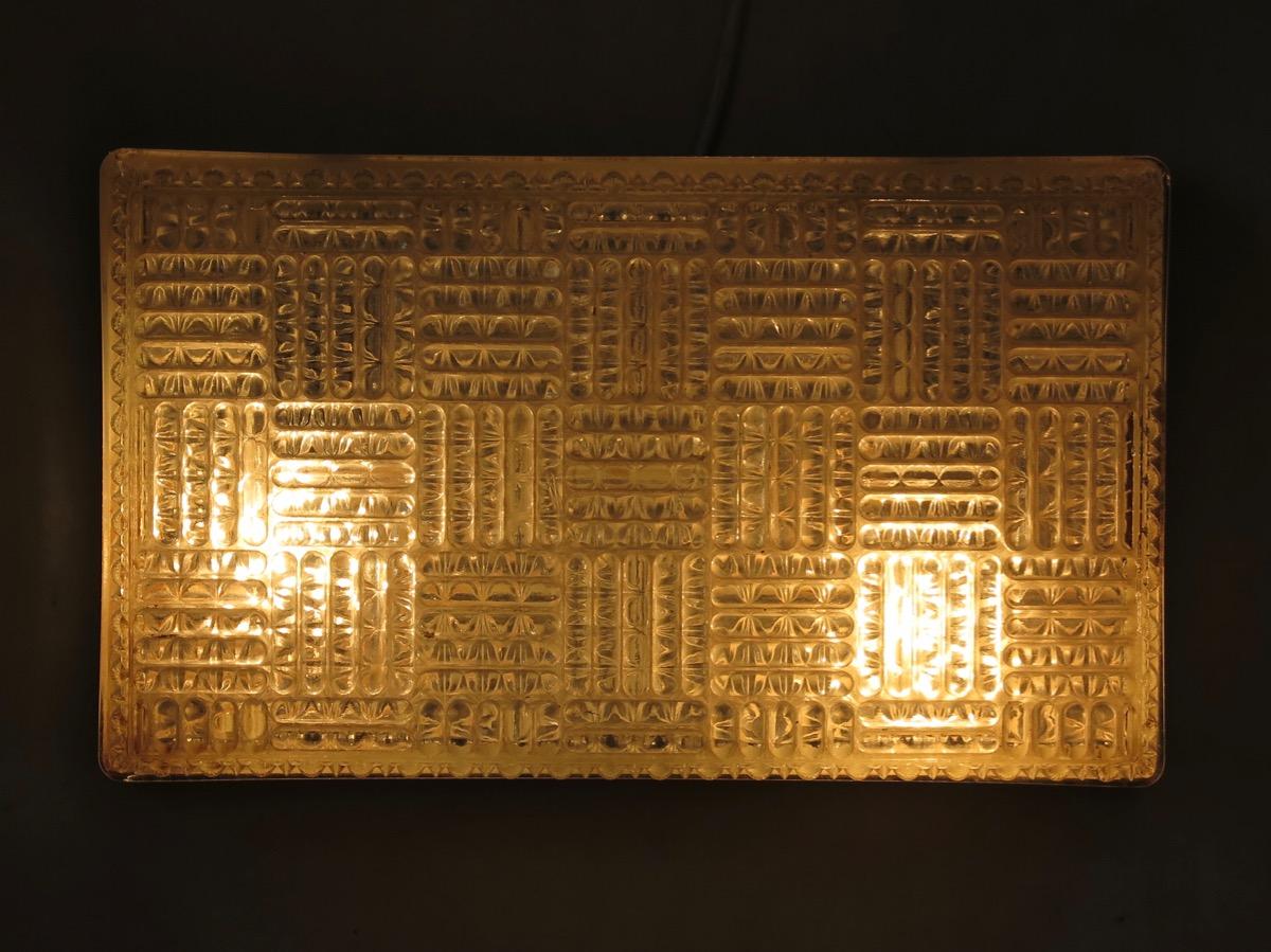 Large rectangular pressed glass wall lights with a geometrical pattern on the surface. Mounted on a metal base, painted black. Each sconce holds two bulbs.
