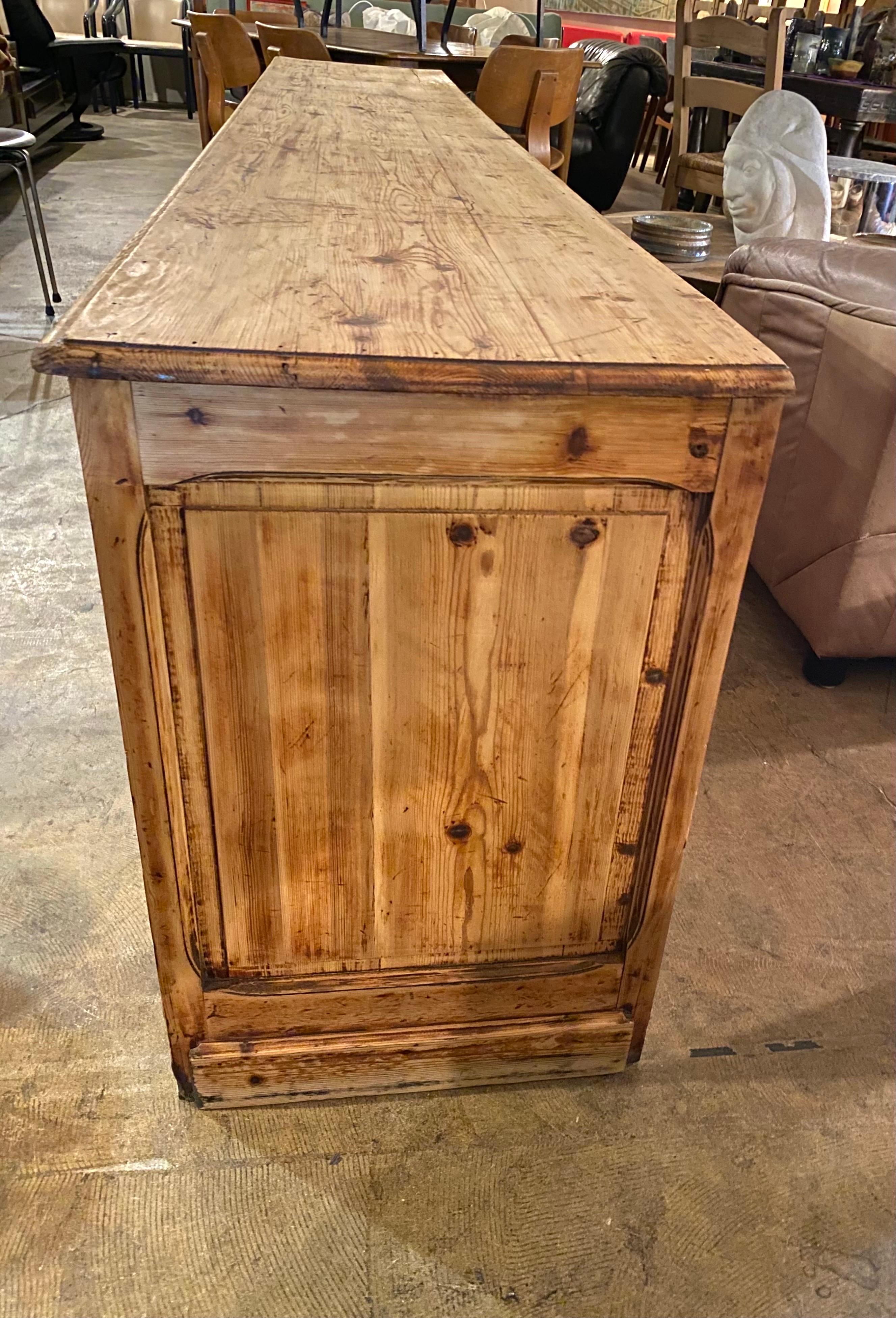 Large primitive credenza is made of pine that has been stripped. Pine credenza has three doors that open to two large spaces for storage, there is no shelving and doors have wooden pulls. This sideboard is sturdy and in good vintage condition,