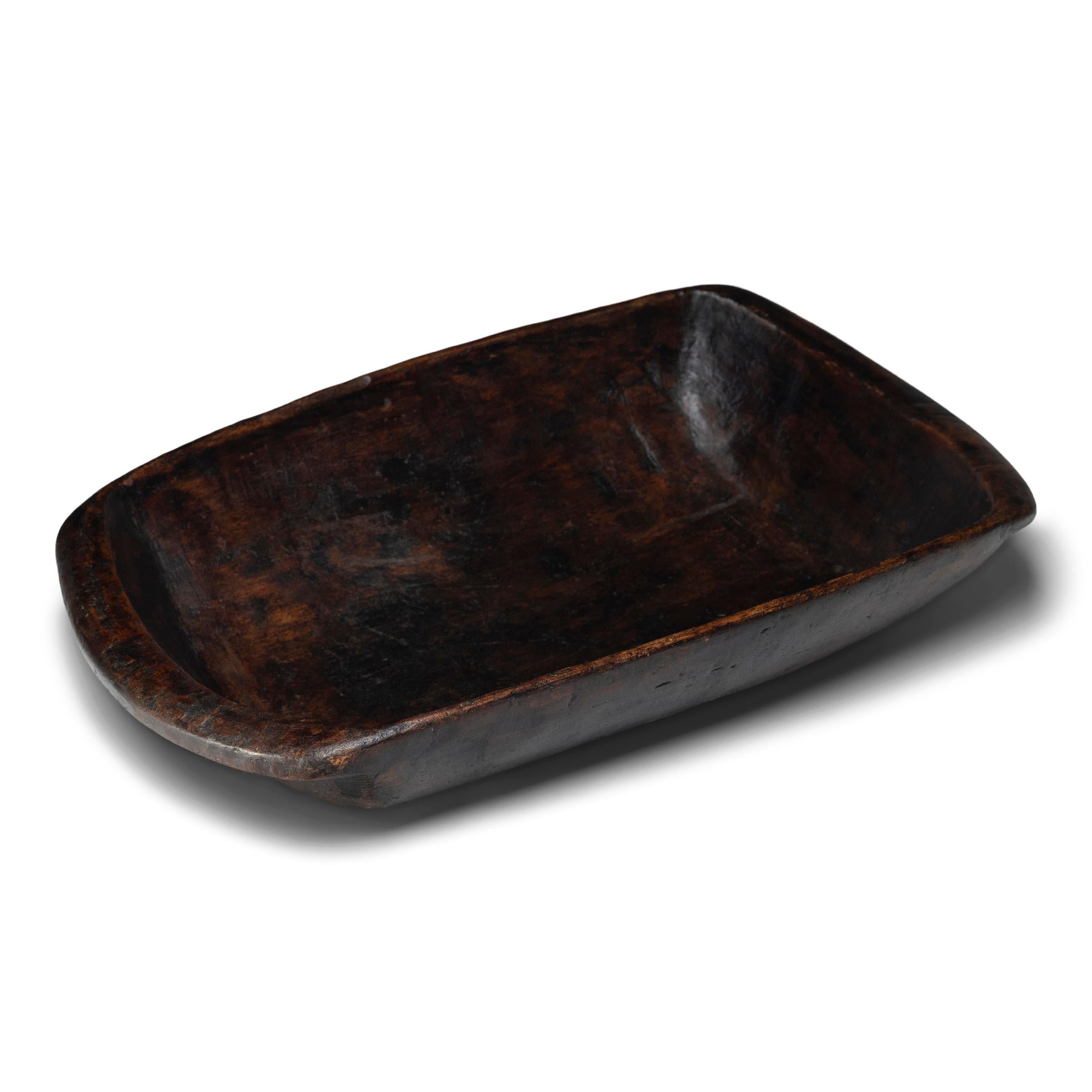 This large wooden farm tray from perfectly balances rustic texture with minimalist simplicity. Carved from a solid block of wood, the tray has a rectangular shape with rounded corners, a deep interior basin and tapered ends that flatten into