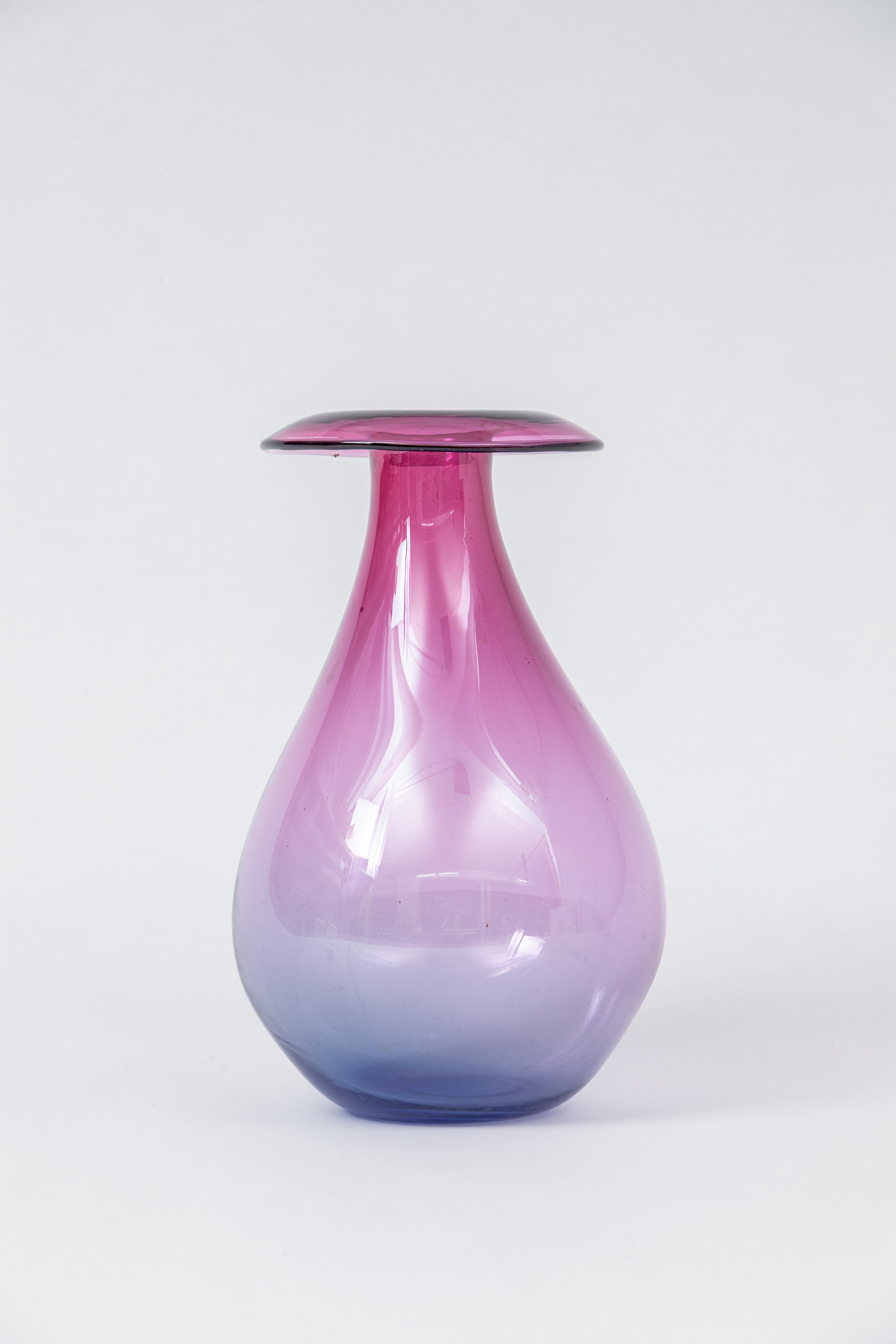 A large murano blown glass vase with a gradient of shades of purples and blues. It is very delicate with a fairly sized neck and lip, and it would make an elegant object or bud vase.