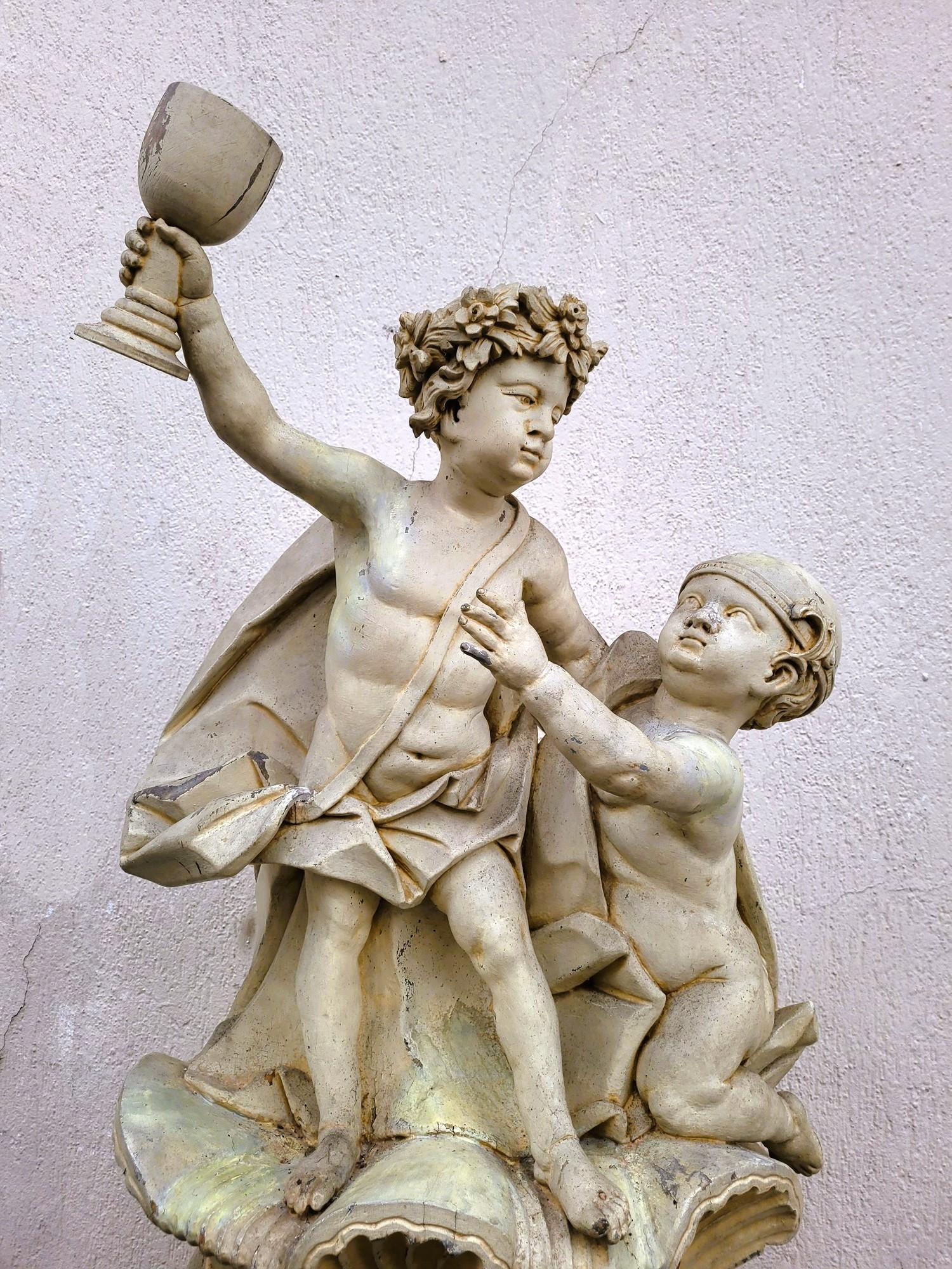 Grande scultura in legno intagliato laccato crema, che rappresenta 2 putti su un grande vaso, che celebrano un baccanale: uno di loro ha la testa circondata da una corona di fiori e brandisce una coppa che il suo compagno cerca di prendere. 

Opera