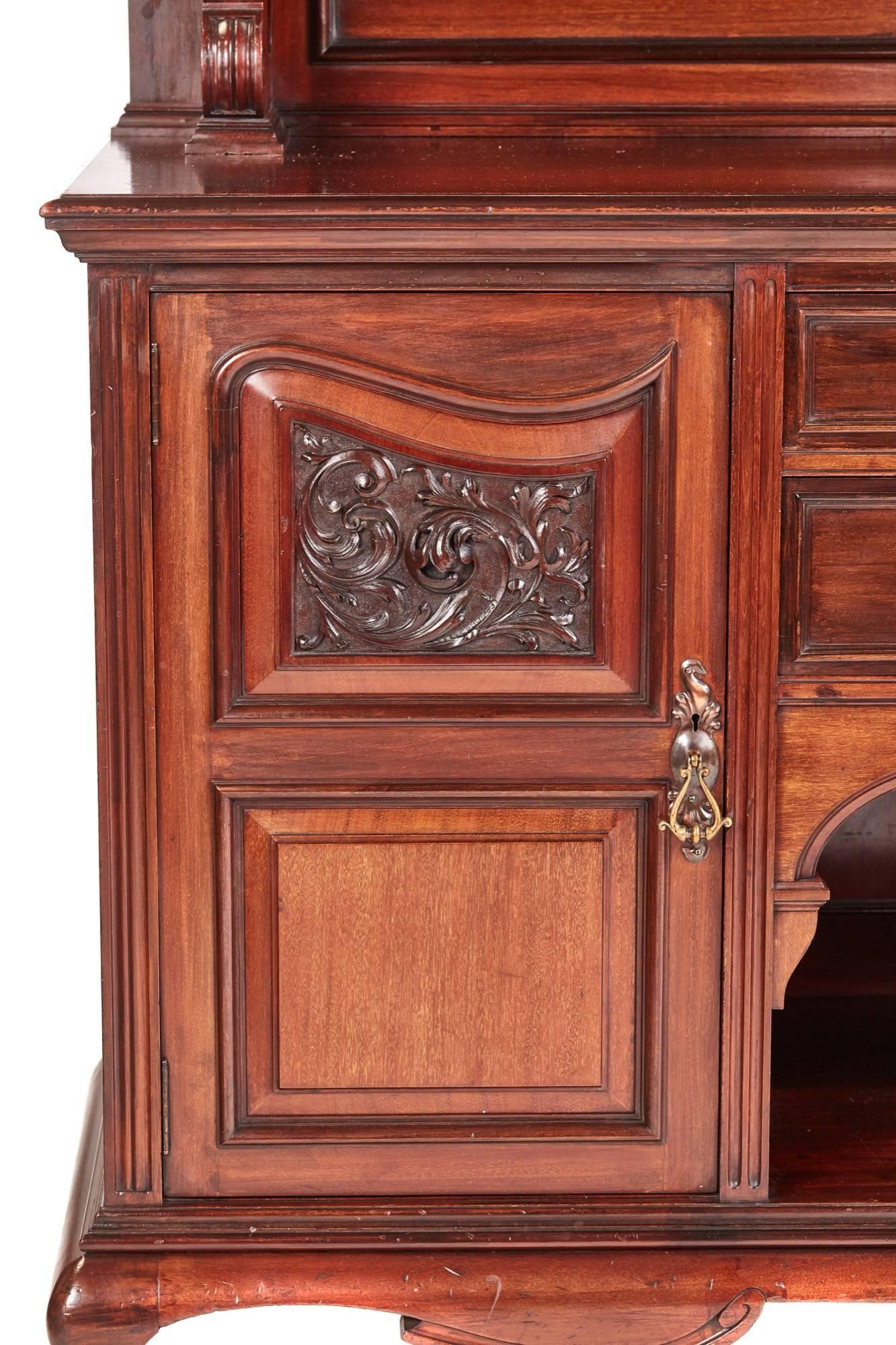Large quality antique carved mahogany sideboard by Maples, the arched mirrored back with projecting flanking fluted columns, the base with two central drawers and recessed shelf below flanked by pair of carved panelled doors enclosing shelves and