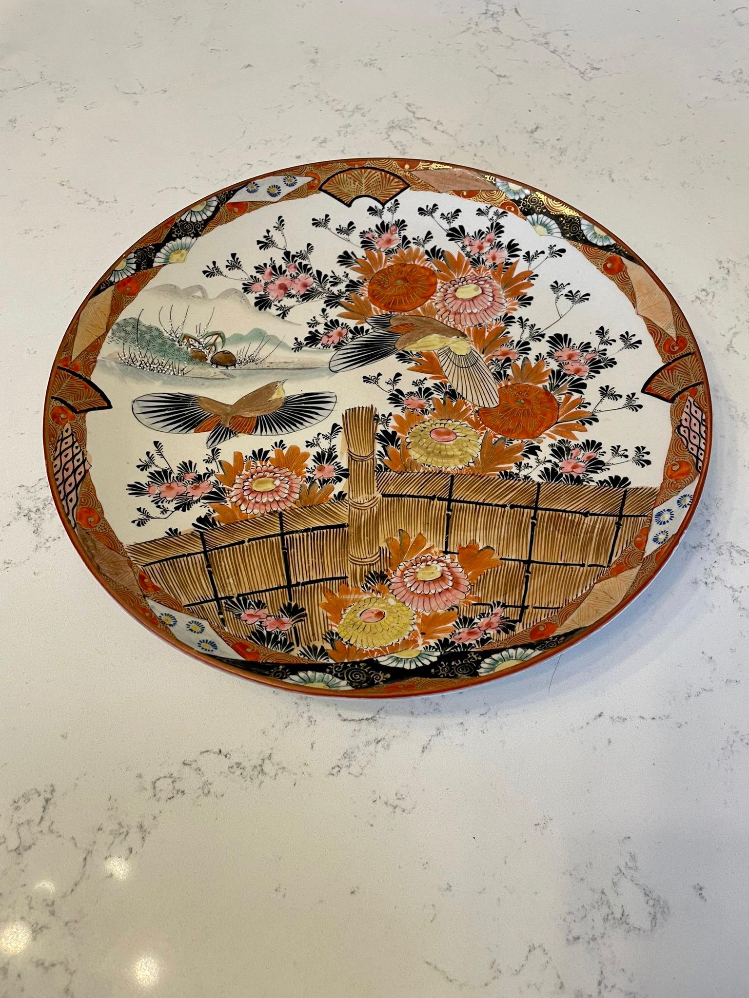 Large quality antique kutani hand painted shallow bowl signed Shozo having fantastic quality hand paintings of a garden with flying birds, flowers, leaves and a golden fence with mountains in the background. It boasts spectacular gold, red, orange,