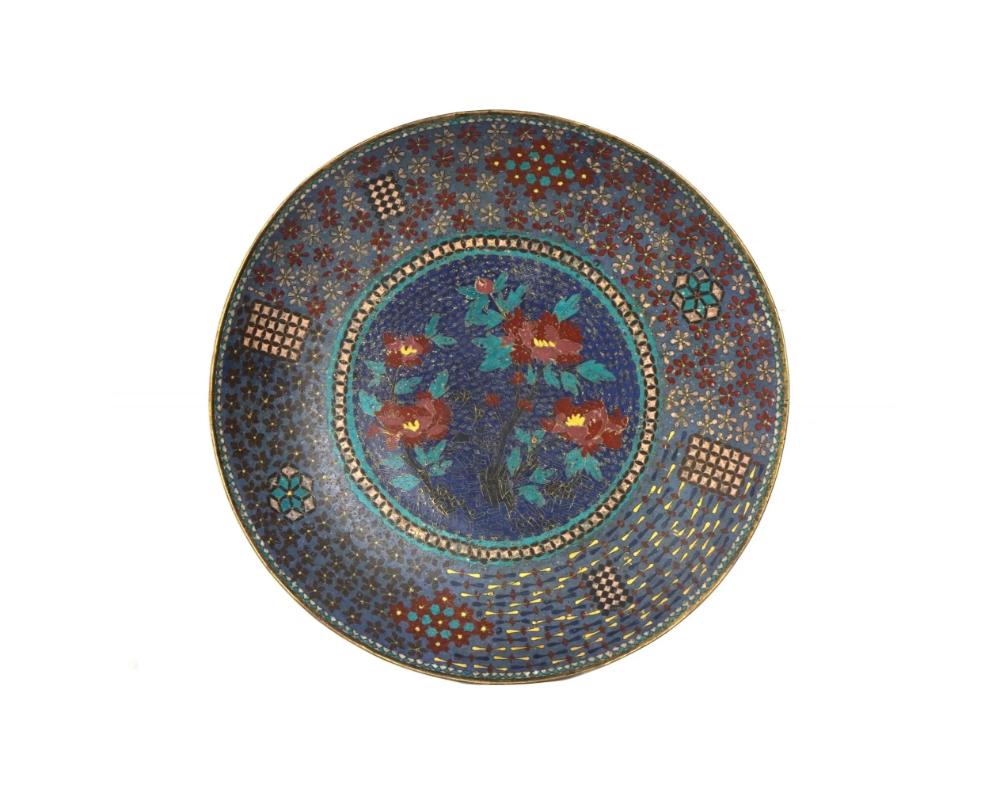 Un grand plateau ou chargeur japonais ancien, de l'ère Meiji, en émail sur cuivre. L'intérieur de l'assiette est orné d'une image en émail polychrome de fleurs épanouies entourées d'ornements floraux et géométriques réticulés sur le fond bleu des