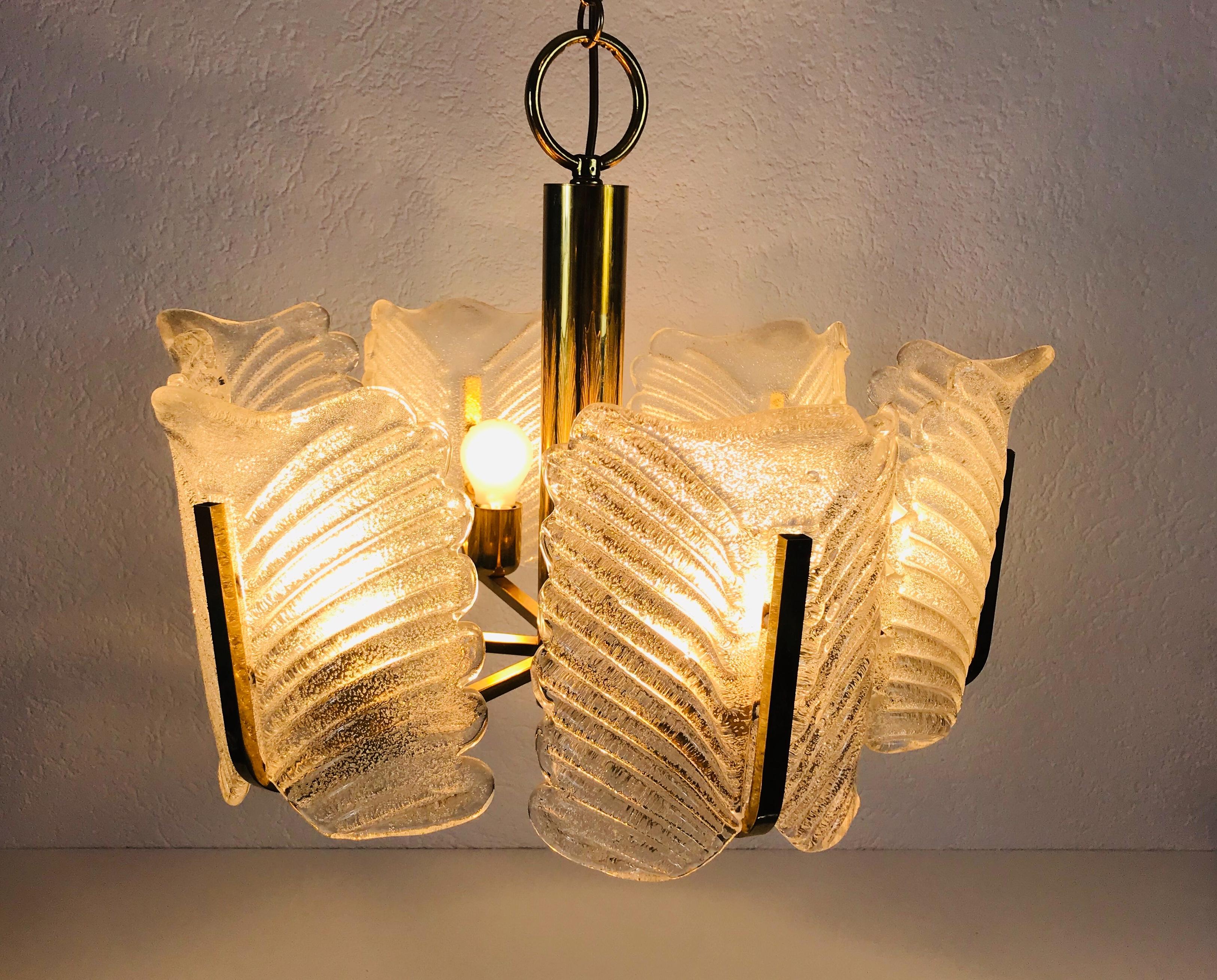 Mid-Century Modern brass chandelier made in the 1960s. It has brass arms, each with an ice glass shade in extraordinary shape. 

The light requires eight E14 light bulbs.