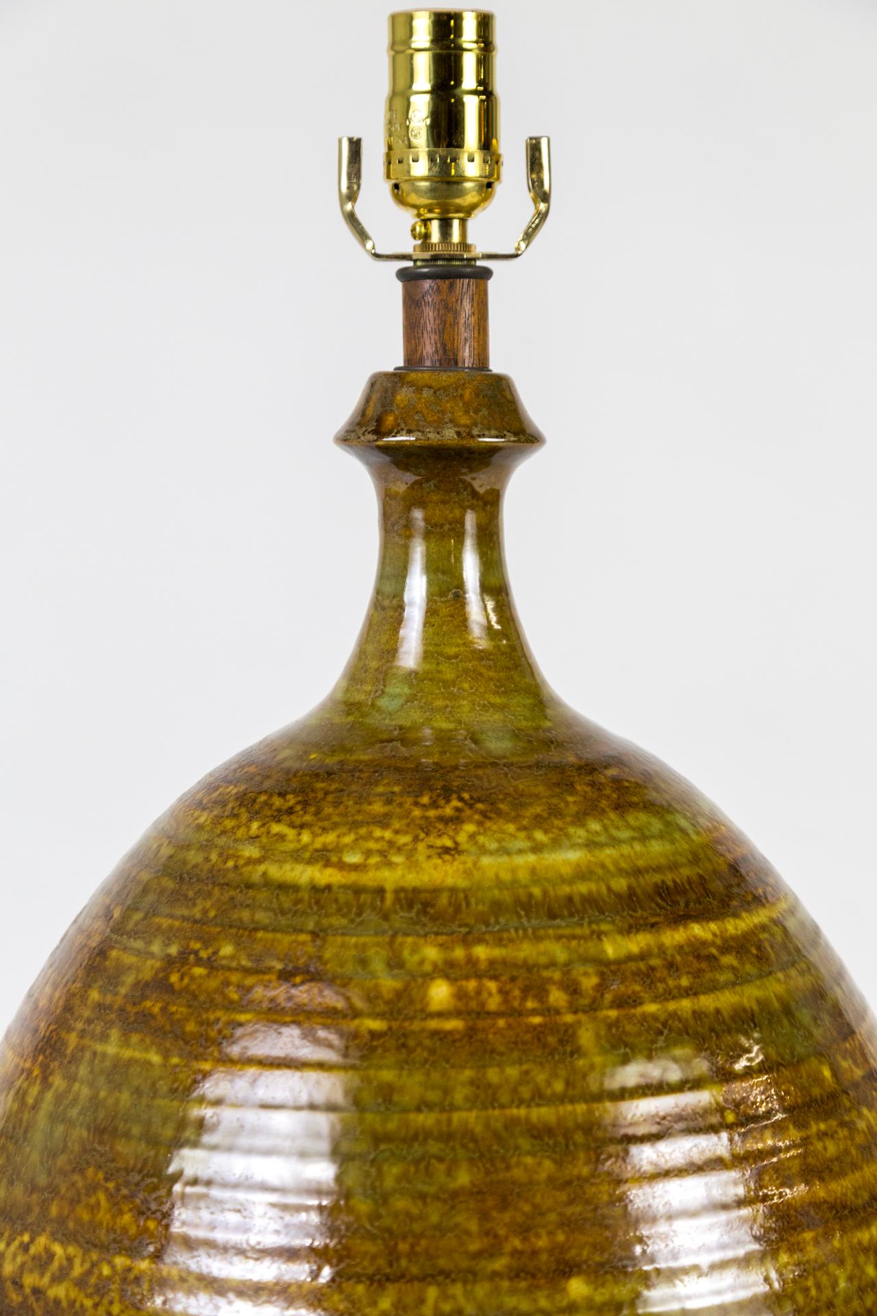 A large, egg shaped, ceramic lamp with horizontal ribs with golden umber and olive green glaze. Accented with wood base and neck, 1970s. Newly rewired. Measures: 27
