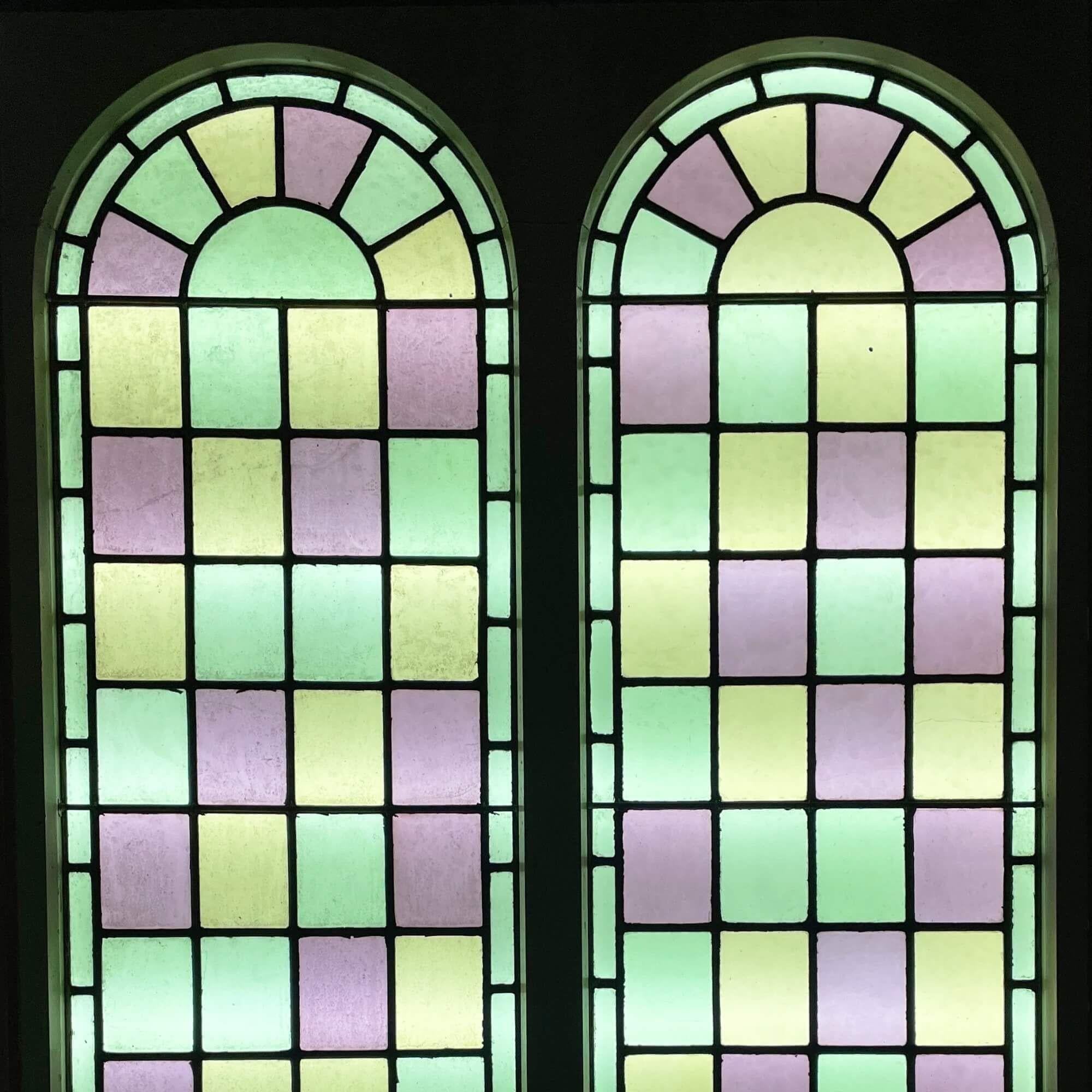 A pair of large reclaimed arched stained glass double windows, sourced from a chapel built in 1850. Tall in scale, these colourful windows are currently fixed into original pine frames. Dating to circa 1880, the panels are decorated in pastel