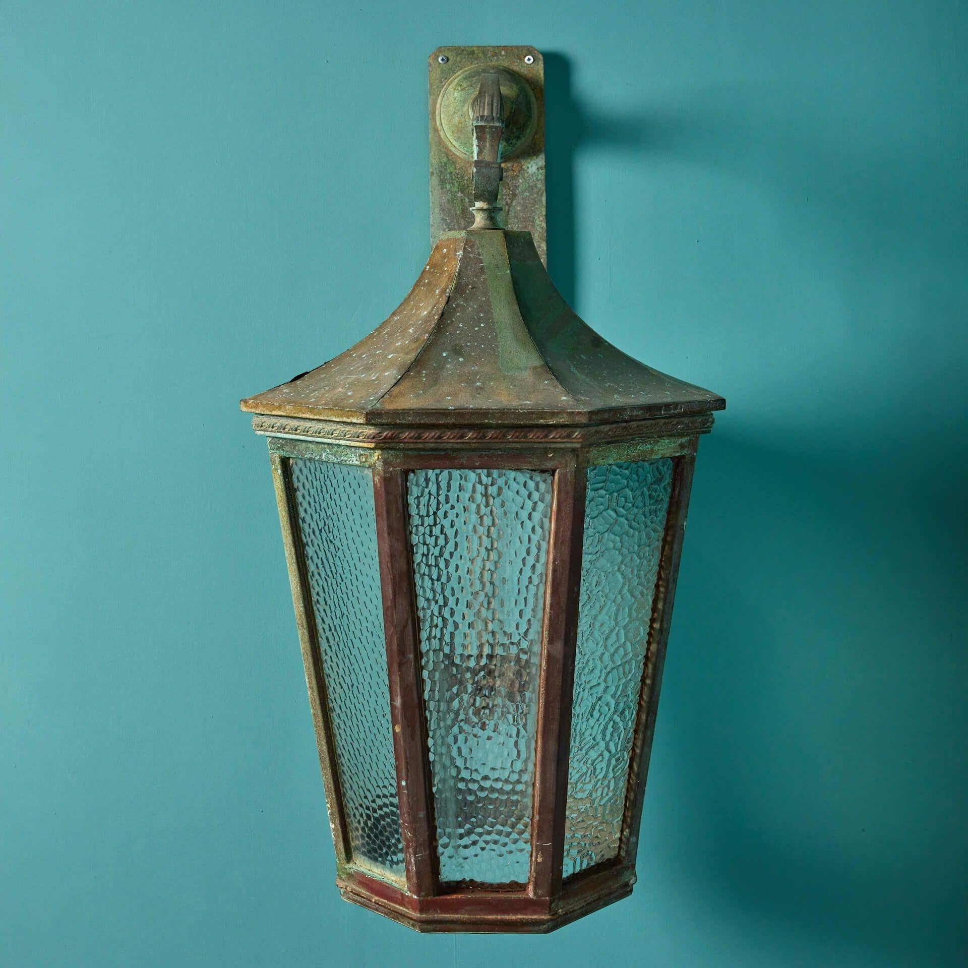 An antique solid bronze wall lantern dating to the early 20th century, suitable for indoor or outdoor use. This lantern is beautifully styled with its weathered bronze creating an unusual eye-catching verdigris patination. The textured obscured
