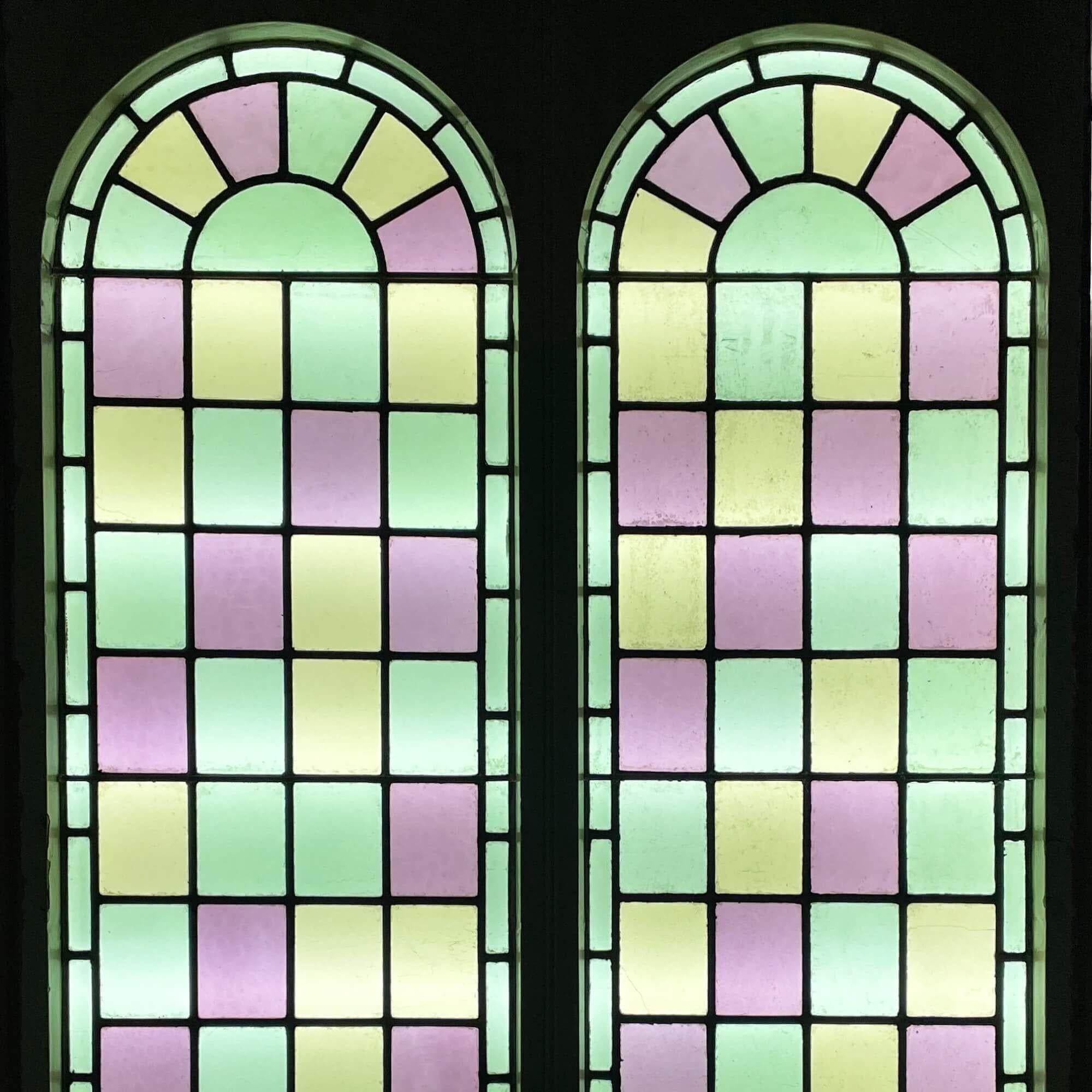 A pair of antique large reclaimed arched stained glass double windows, sourced from a chapel built in 1850. Tall in scale, these colourful windows are currently fixed into original pine frames.

Dating to circa 1880, the panels are decorated in