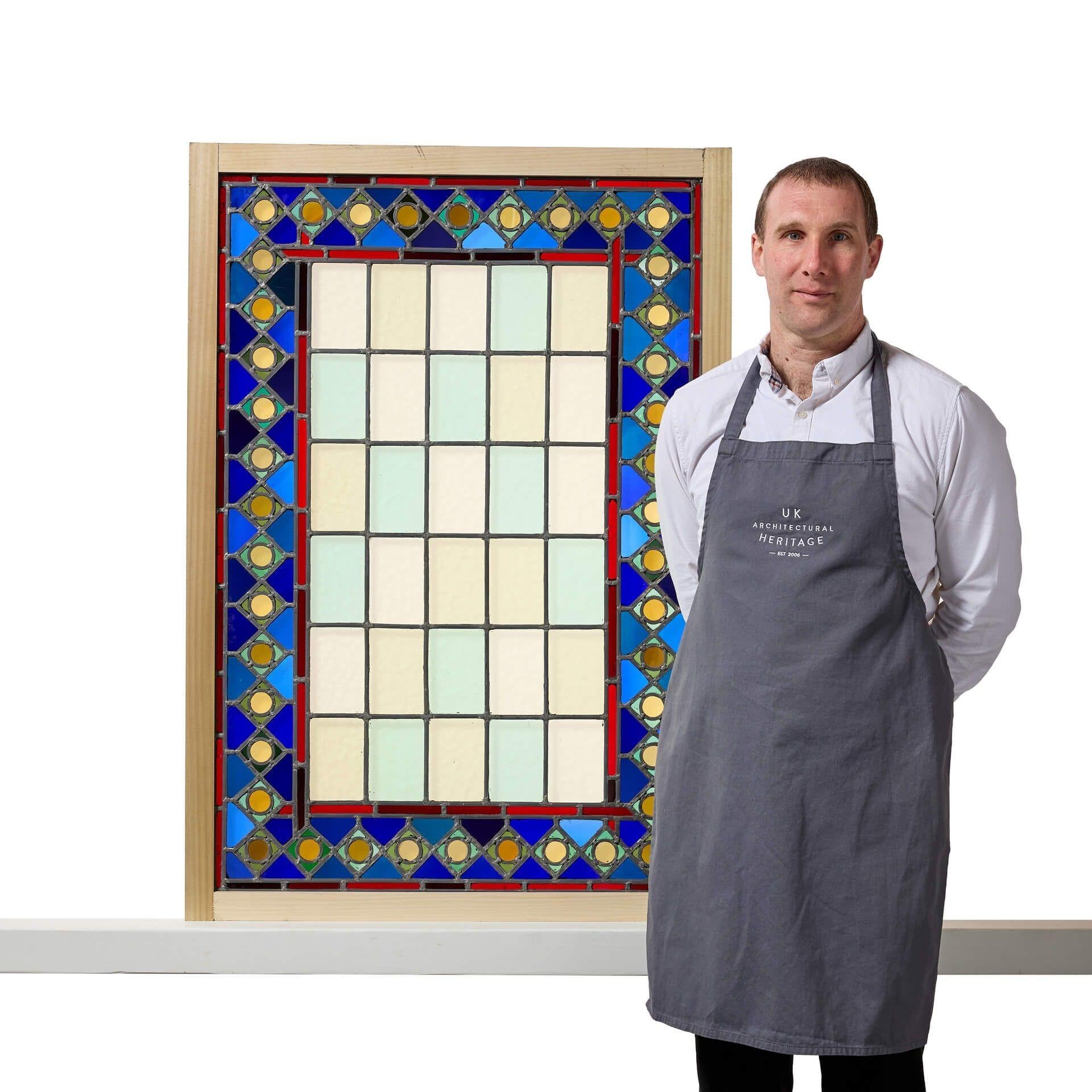 Ein großes rechteckiges Buntglasfenster im mittelalterlichen Stil, eines von drei ähnlichen im gleichen Design in verschiedenen Größen, die wir verkaufen.

Diese Bleiverglasung ist mit ihrem leuchtend blauen und gemusterten Glasrand, den roten