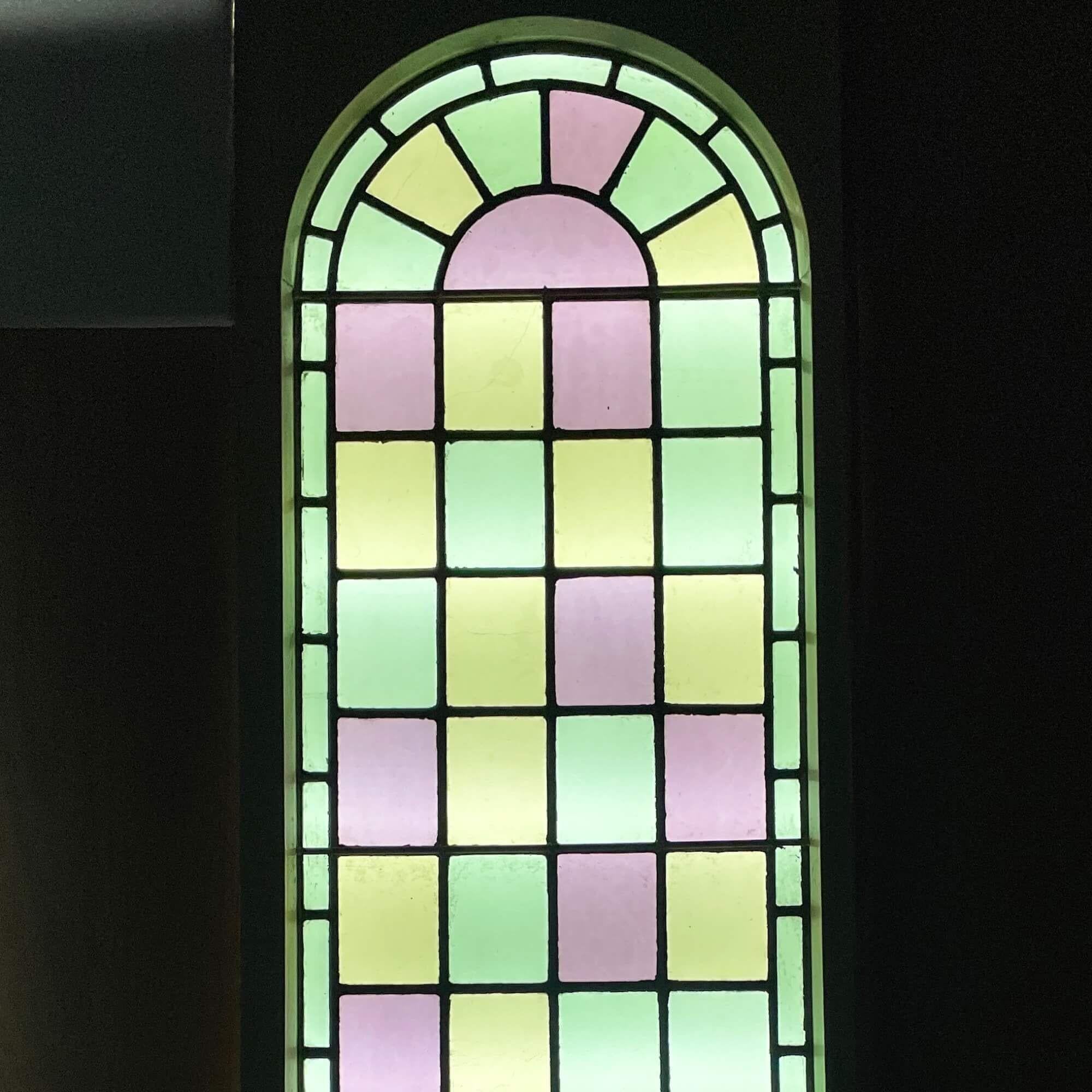 A large antique reclaimed stained glass chapel window sourced from a chapel built in 1850. Tall in scale, the panels are decorated in pastel colours, forming an arch at the top, which would be brought to life by the sunshine of the early morning. At