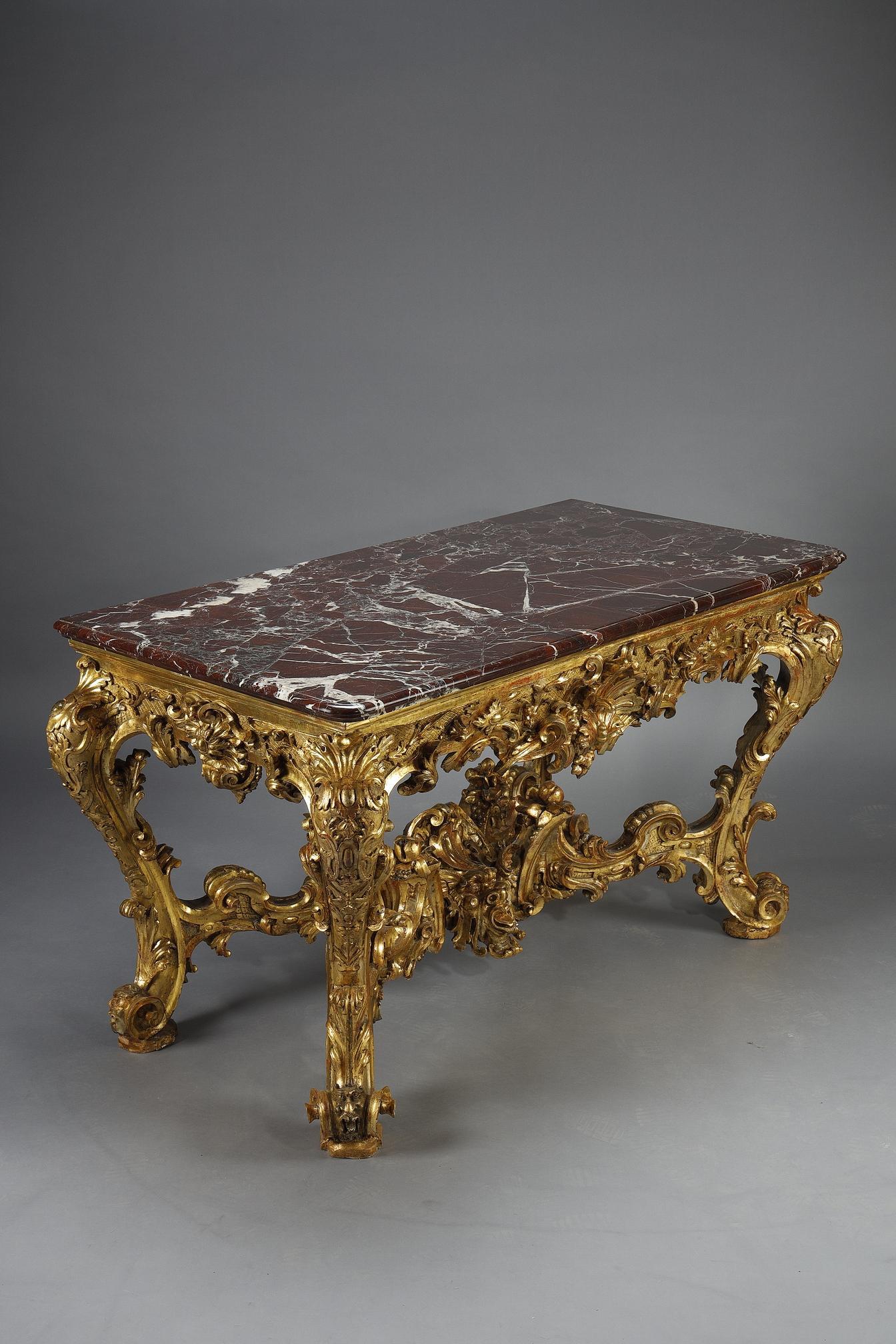 Gran consola rectangular de madera ricamente tallada y dorada. Cinturón ancho decorado con dagrafes, rosetas, conchas estilizadas y follaje. Los montantes y las patas están muy agitados con hojas de acanto, lambrequines y volutas, unidos por un