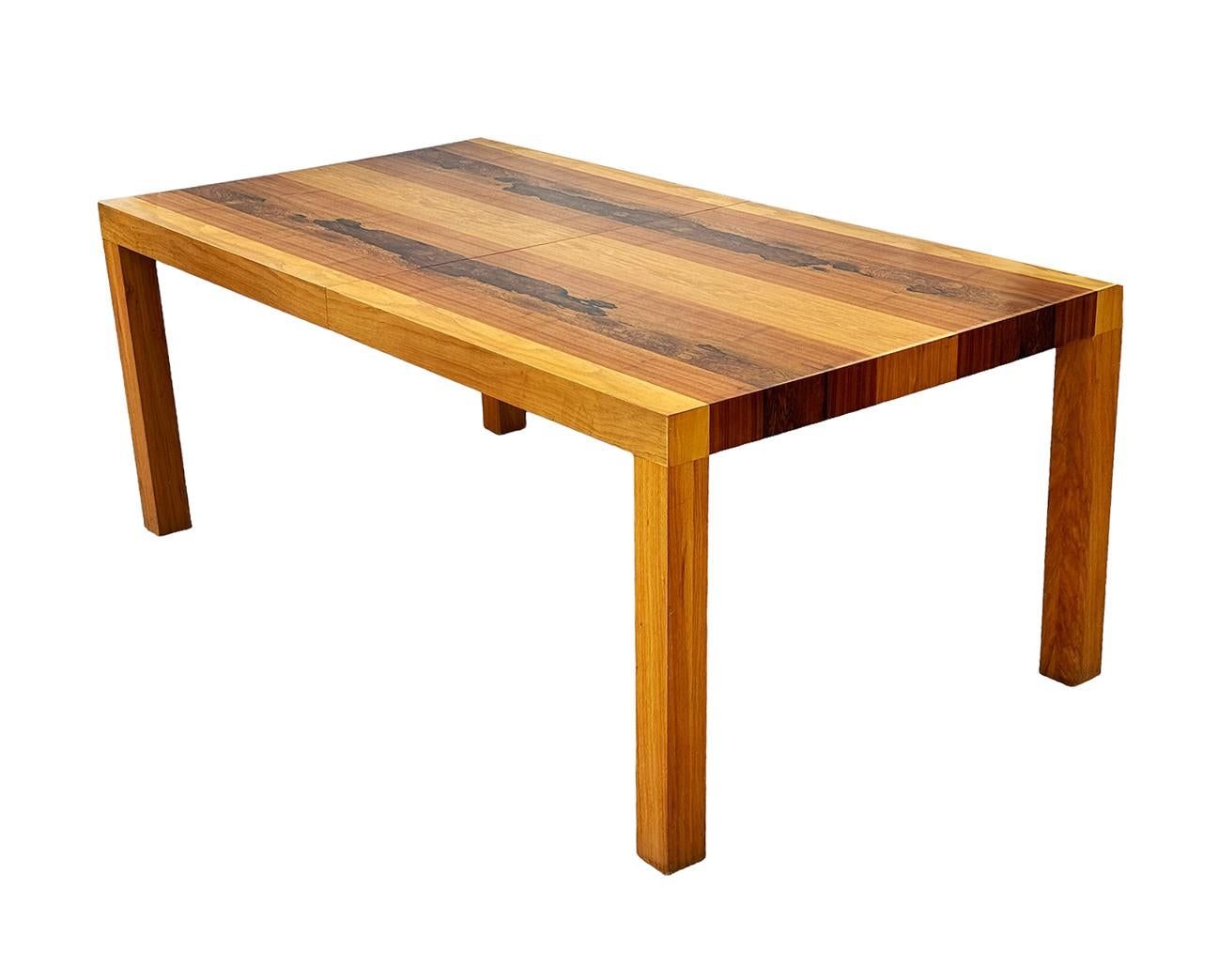 A large and beautifully grained exotic hardwoods dining from Denmark circa 1970's. Its features a large classic Parsons design form. It has one 20 inch extension leaf as shown. The measurements below are for the table without the leaf. The table