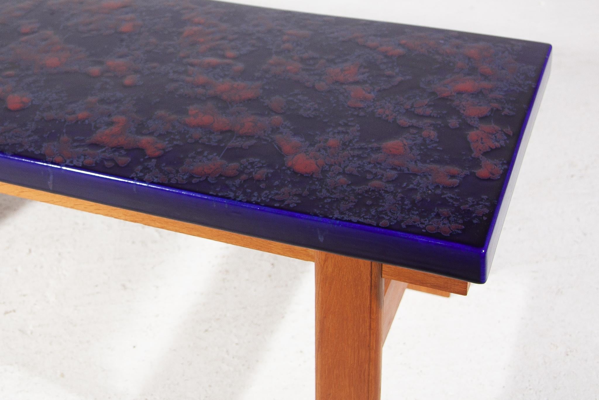 Rare table basse ou table d'appoint originale des années soixante-dix, composée d'un grand carreau de céramique émaillé d'un bleu vif avec des accents contrastés de taches orange qui font de la table un bel objet chaleureux dans votre intérieur. La