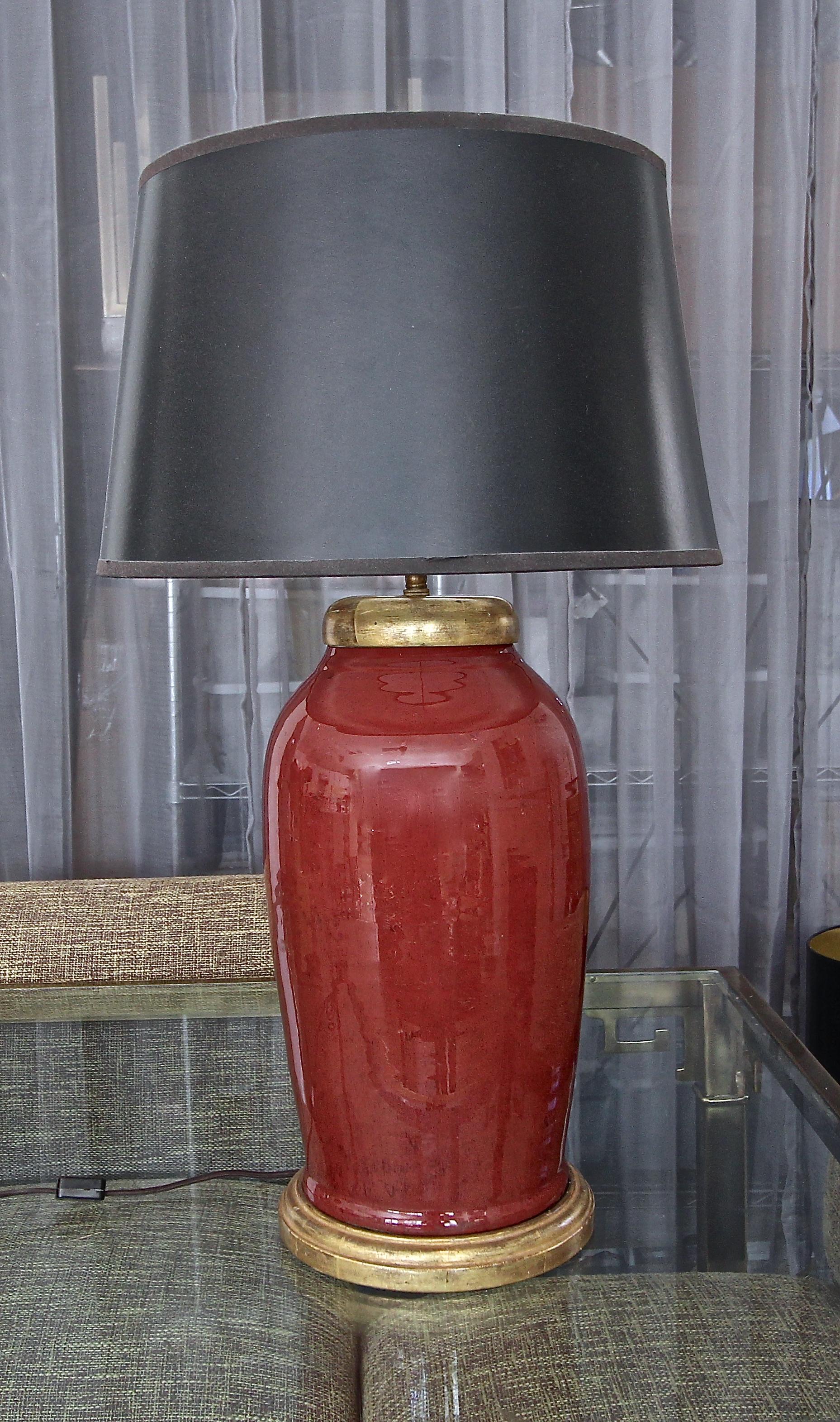 Large single) oxblood (red) porcelain vase table lamp, mounted on 23-karat water giltwood base. Interior vase cap is also turned wood in a 23-karat gilt finish. Antiqued finish hardware includes double sockets with on/off pull chains, adjustable