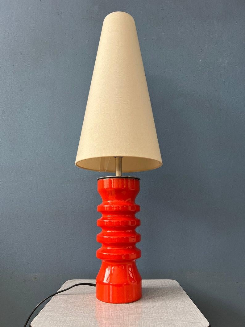 Grande lampe de table en céramique rouge avec abat-jour en textile beige. Le socle en forme de lave grasse est recouvert d'une épaisse laque rouge. La teinte produit un éclat chaud et confortable. La lampe nécessite une ampoule E27/26 et dispose