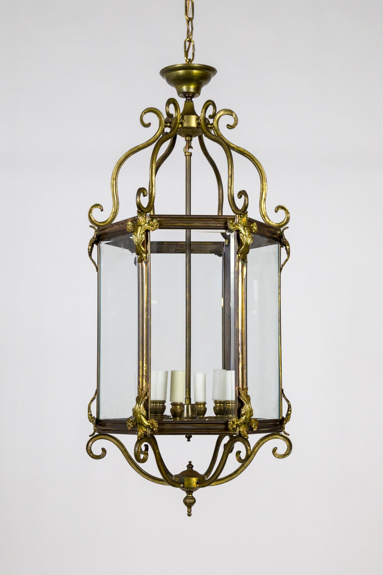 A large, brass lantern with six, beveled glass panels with scrolls at the bottom and top. The finish has a beautiful bronze tone with acanthus leaf accents and floral bobeches; 6 lights. 73