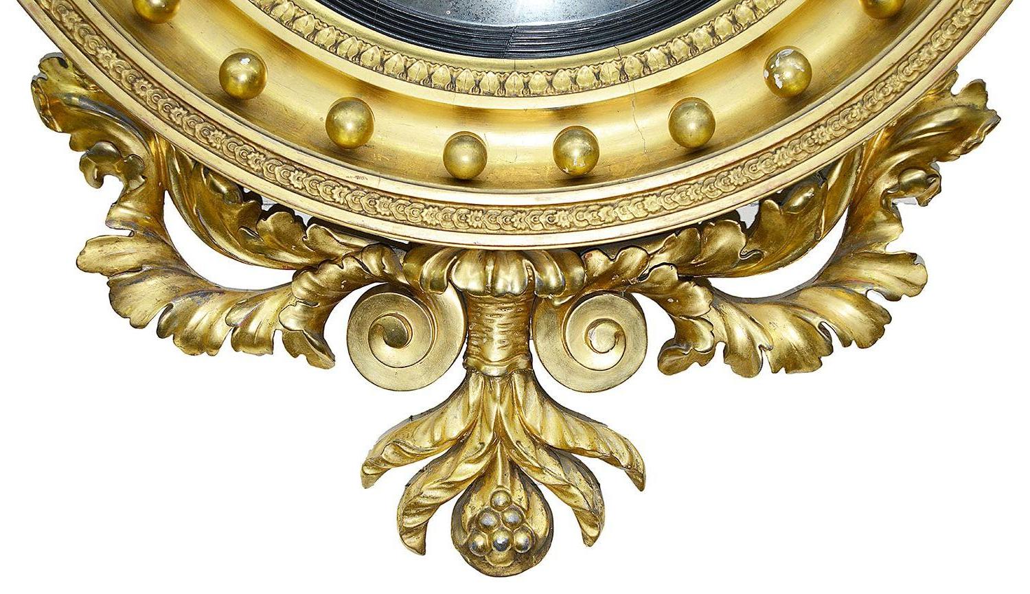 A large and impressive early 19th century Regency period gilded convex wall mirror, having a carved giltwood eagle above scrolling leaves and cornucopia, an ebonised slip around the convex mirror, gilded balls and carved foliate decoration to the
