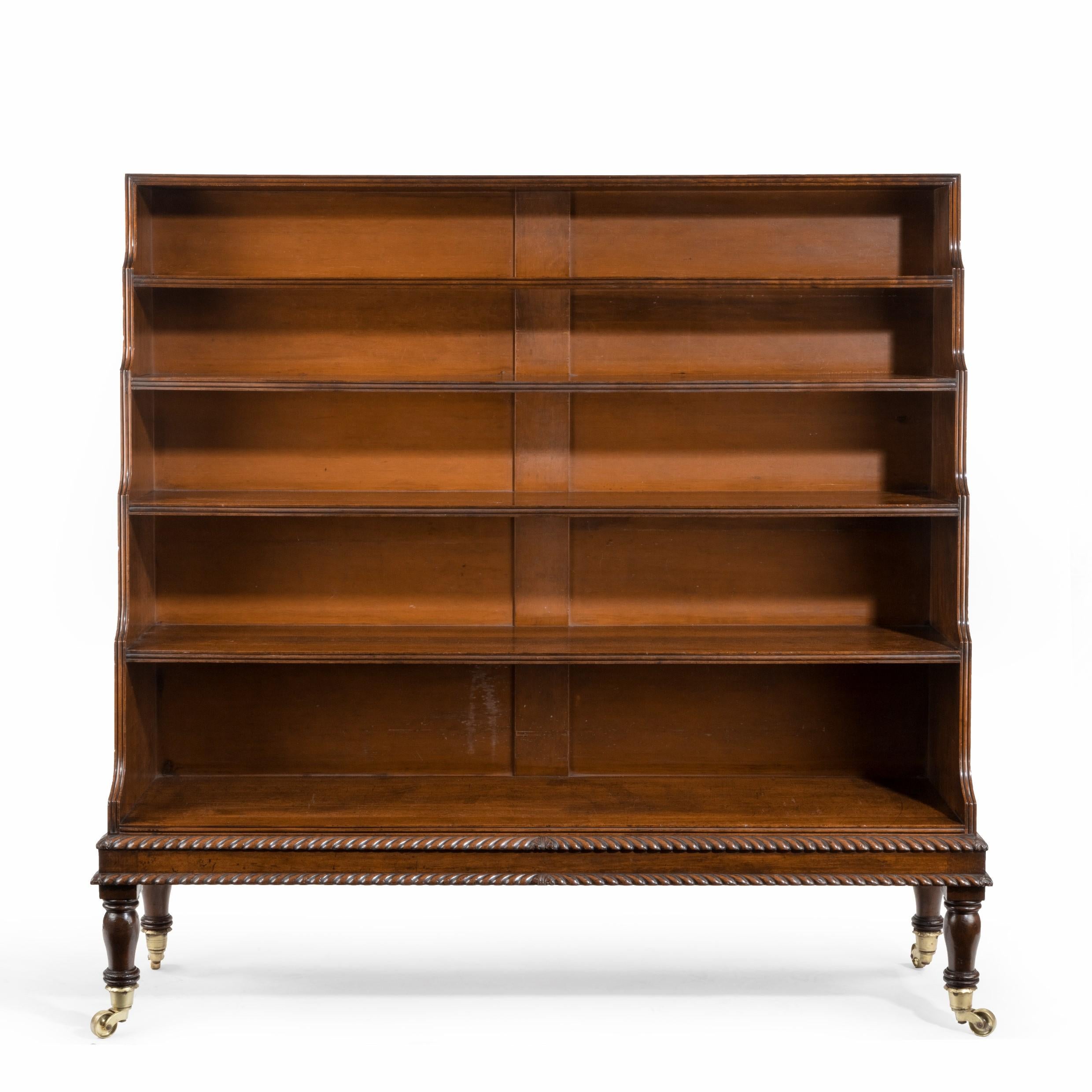A large Regency mahogany waterfall open bookcase, of upright rectangular form with five graduated shelves raised on turned baluster legs with brass handles and castors, decorated with reeding and two bands of gadrooning. English, circa 1820.
 