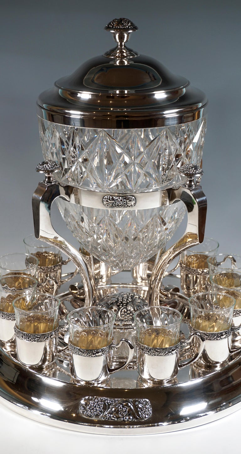 Large representative punch bowl in elegant silver fittings:
Large circlet with a square cross-section supported by four high, curved legs with volute feet on a round, profiled pedestal, which also offers a place to put the 12 blown glasses in large