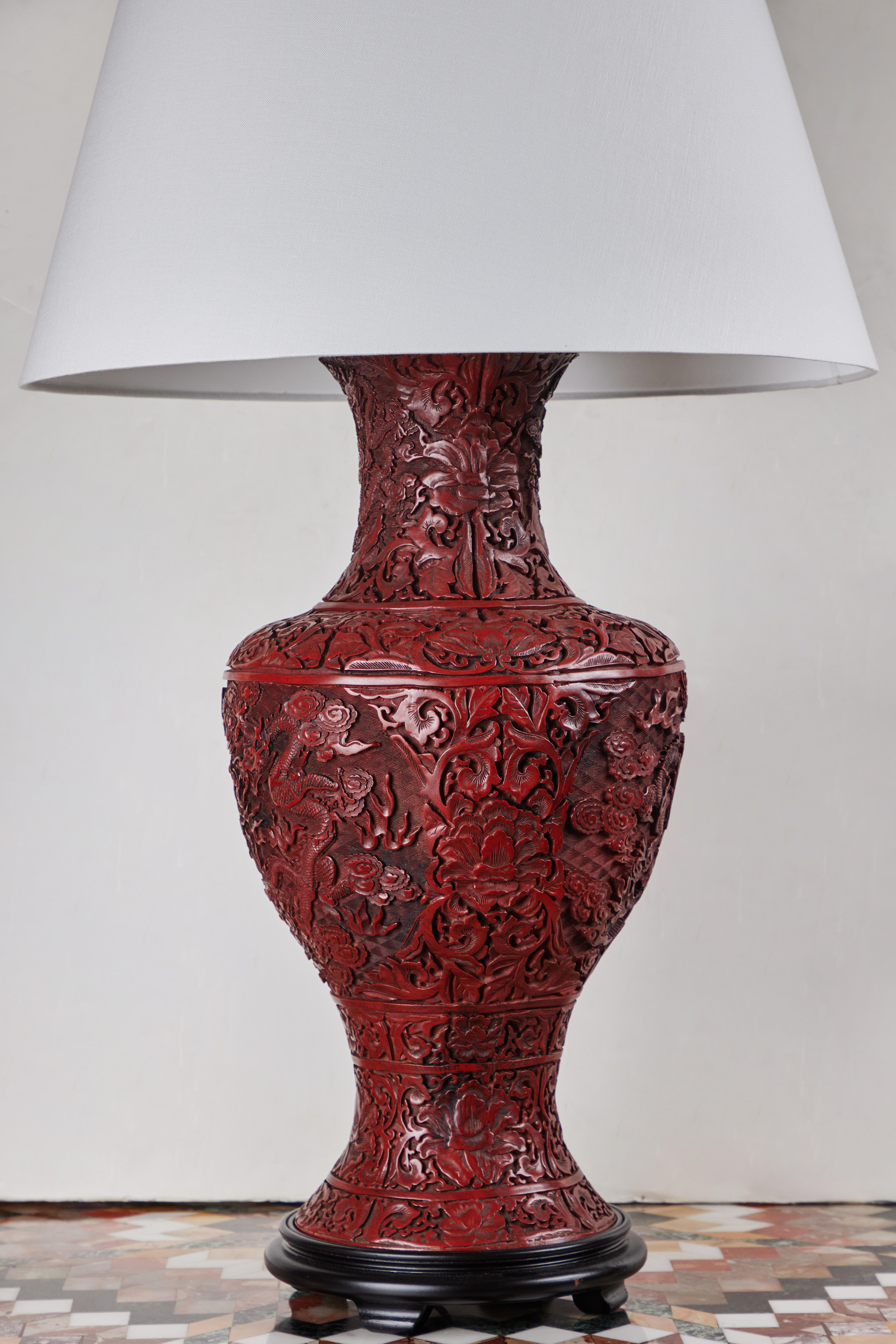 An elaborately carved pair of grand-scale, Chinese, Cinnabar vases turned to table lamps. Each fully decorated with chrysanthemum blossoms, foliate forms, and sinuous dragons among clouded skies.  Newly wired for U.S. current. Shade diameter: 21.75