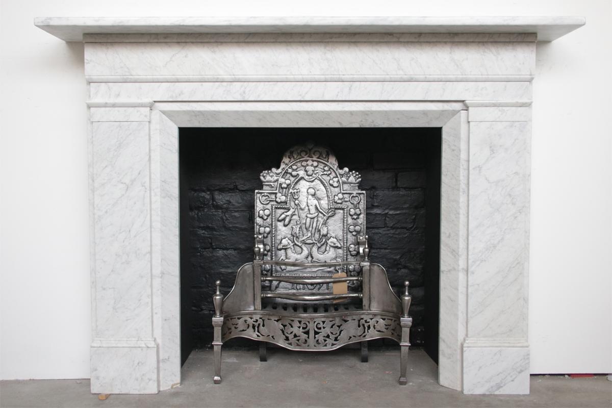 A large restored antique early Victorian Carrara marble fireplace surround of simple form with a full-width frieze above plain jambs with chamfered inside returns. English, circa 1840-1850 Pictured with a 19th century cast iron and steel dog grate,