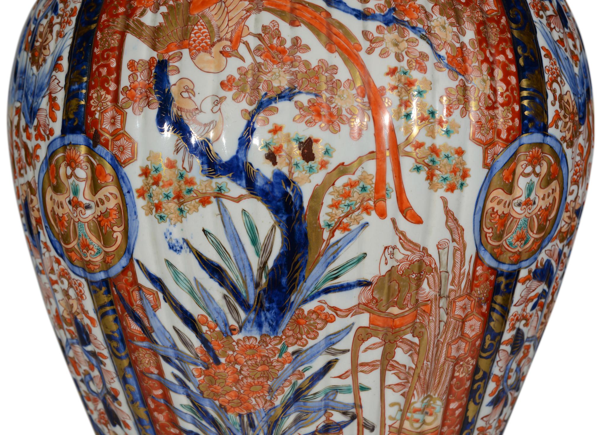 Magnífico jarrón Imari japonés del siglo XIX, de gran tamaño, con cuerpo acanalado, decorado en su totalidad con la típica paleta Imari de rojos y azules férreos con reflejos dorados sobre fondo blanco, con dos grandes paneles que representan