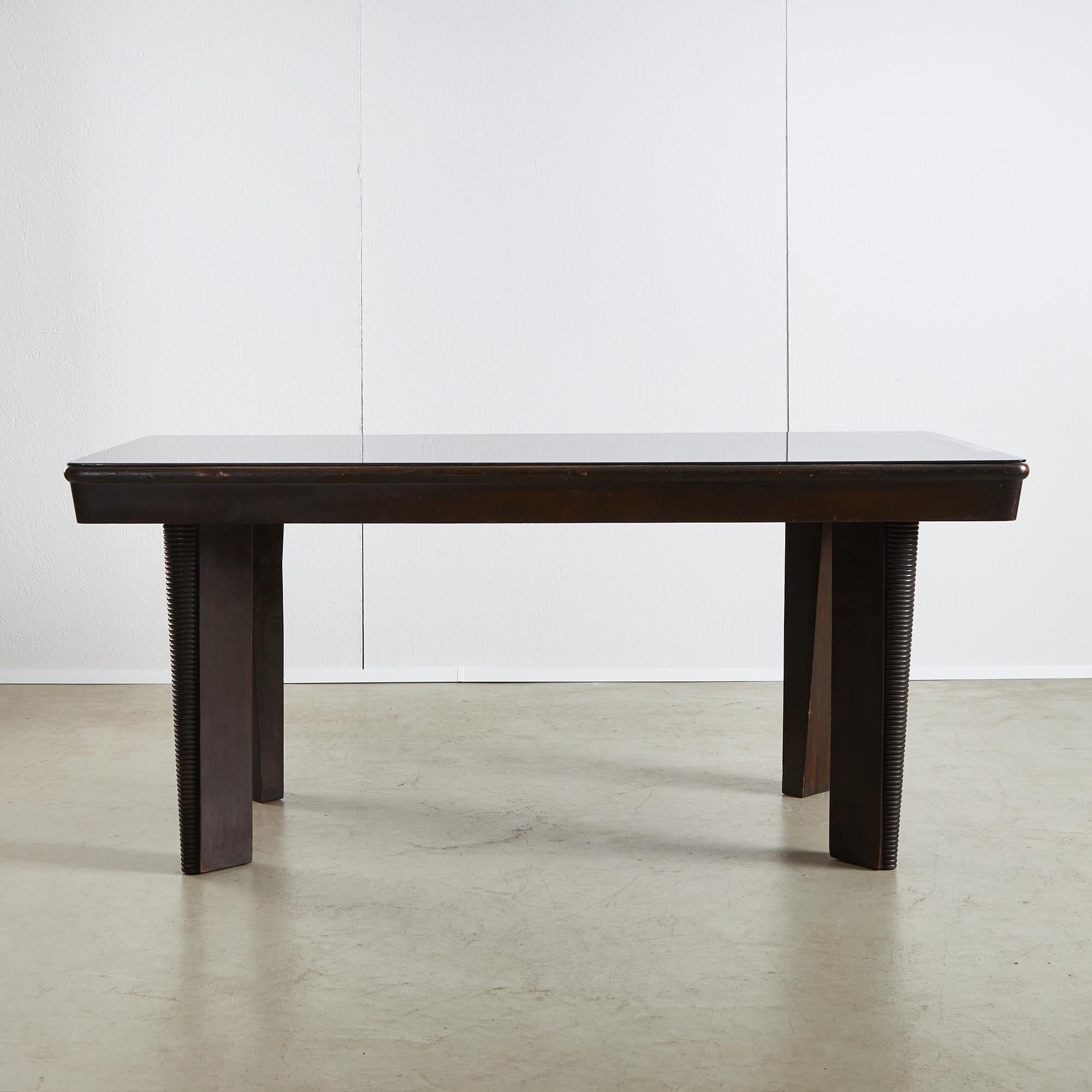 La table de salle à manger en question est une pièce d'artisanat remarquable, présentant un ton de bois foncé profond et riche qui témoigne de son histoire et de son savoir-faire. Peint à l'origine dans une finition noire épurée, le bois a subi