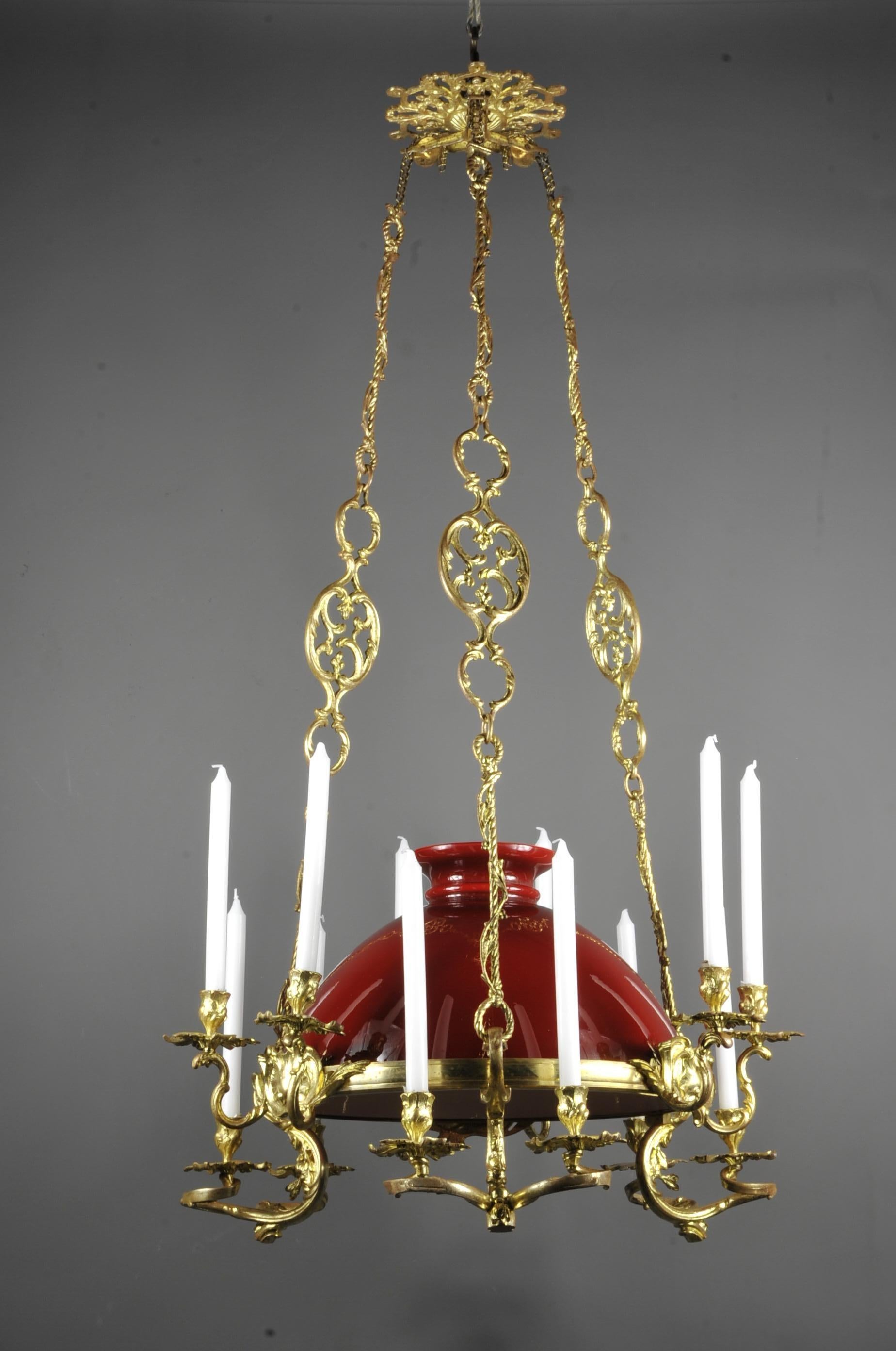 Imposing gilt and chiseled bronze chandelier with 12 belt lights in ornaments of volutes, shells and acanthus foliage of rockery inspiration.
In the center a large dome lampshade in red opaline with a white interior, the whole is suspended by three