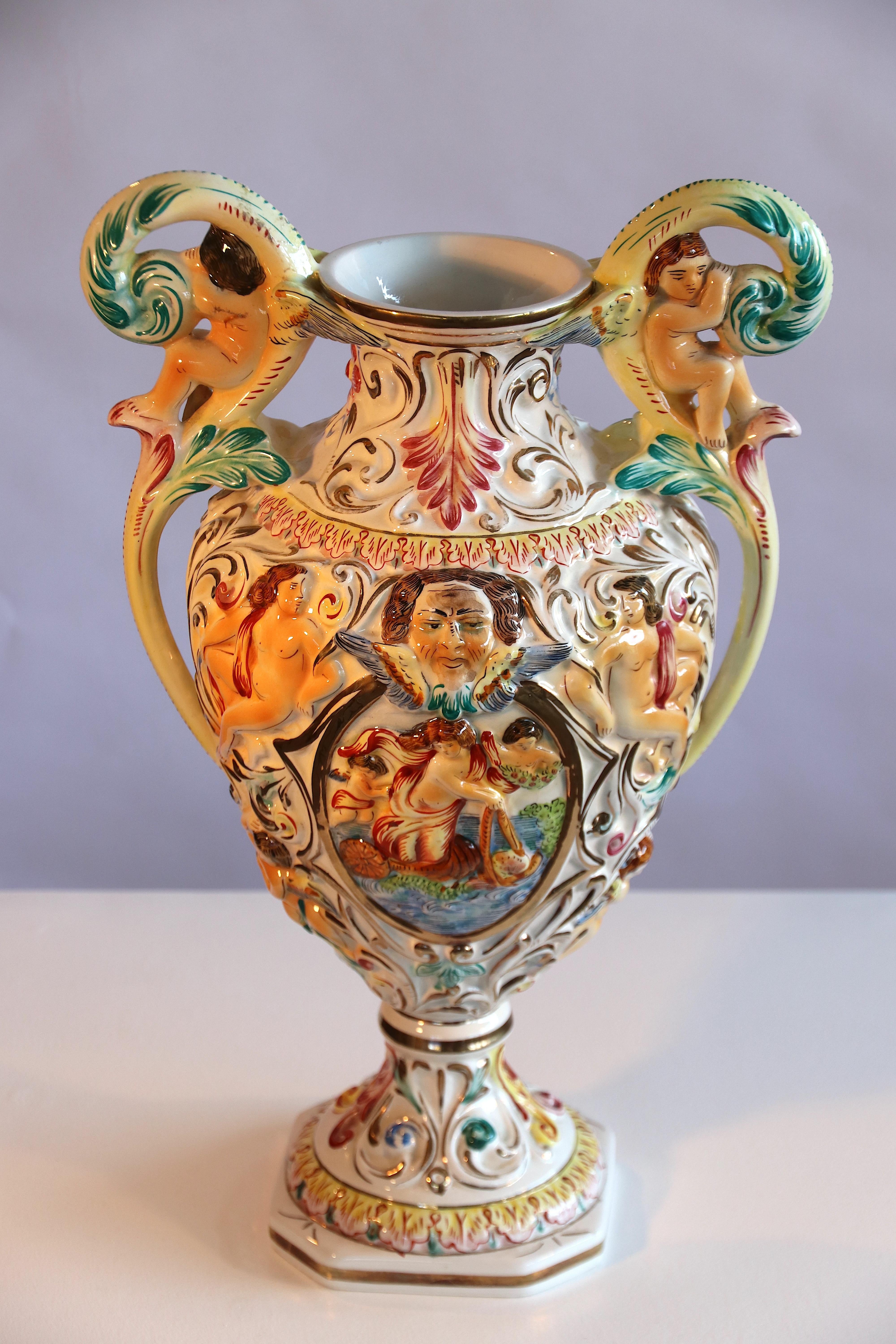 Stunning ornamental raised-relief Rococo style amphora vase with two handles by Capodimonte Naples, Italy, signed on the bottom with the original R. Capodimonte stamp. The vase features 2 cherubs in the handles and several faces, Roman mythology