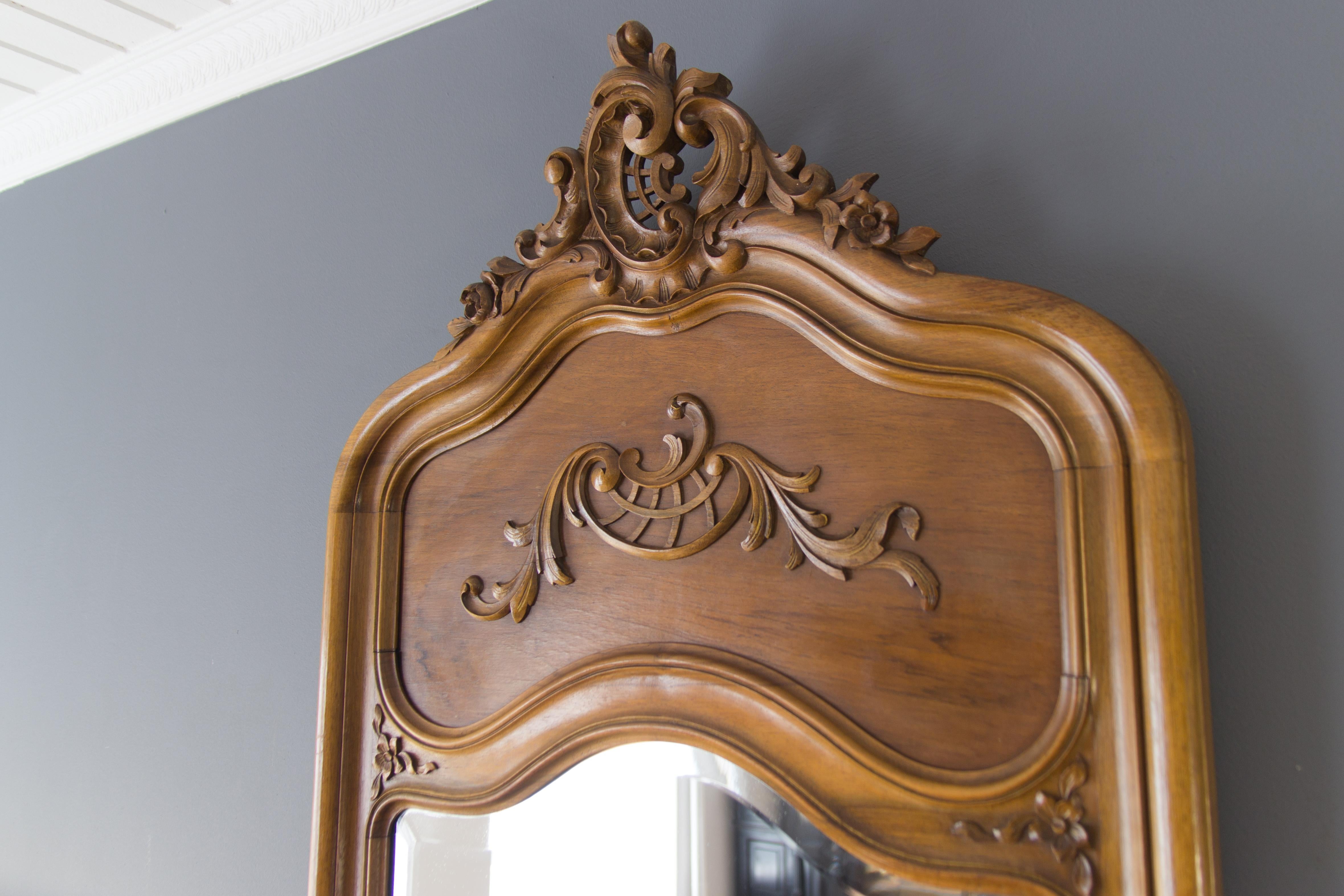 This elegant Rococo style floor mirror features a hand-carved walnut ornate frame with leaf, flower and scrolls details. Nicely shaped and beveled original mirror plate, Belgium, Miroiterie du Brabant, Bruxelles, 19. 04. 1932. 
In good condition,