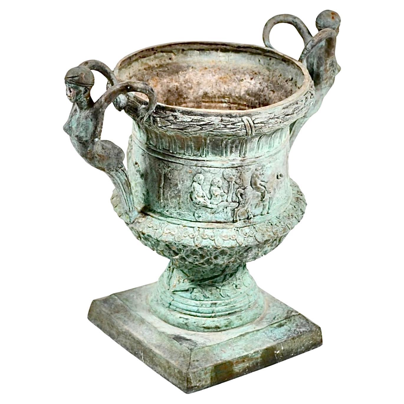 Grande vaso da giardino in bronzo figurato in stile romano. La fioriera in bronzo è caratterizzata da un carro guidato da una mucca con figure su entrambi i lati. L'intricato motivo del bordo a corona simboleggia l'onore o l'eternità. Le maniglie a
