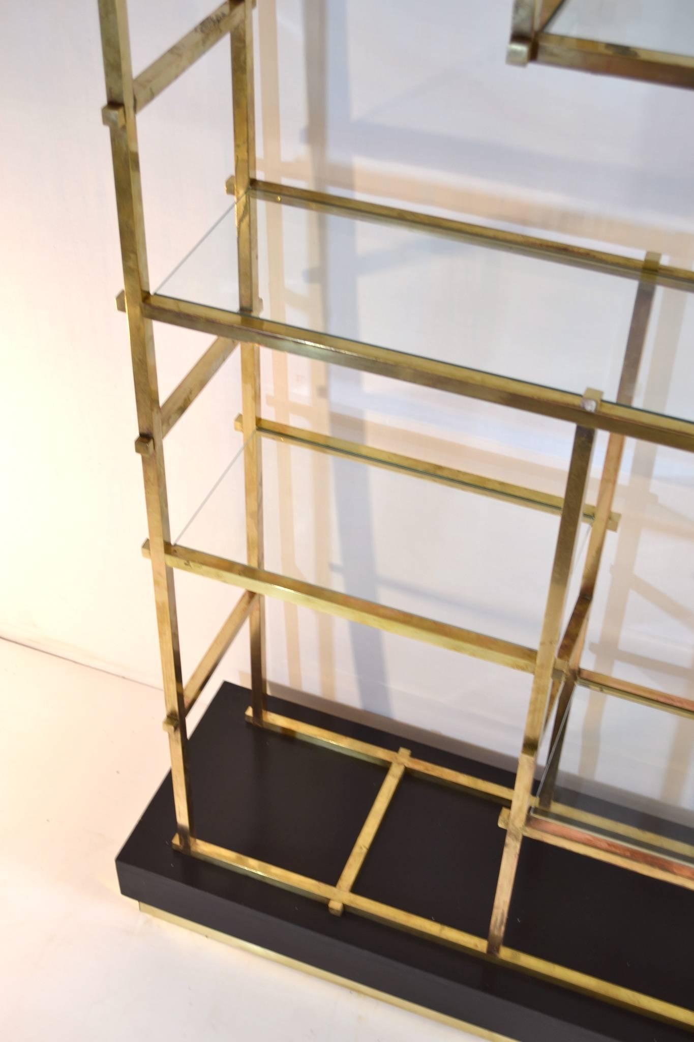 Super stylish shelf/étagère´ in brass with clear glass shelves standing on a black wood base with brass trimming. The shelf is very characteristic and held together with large square brass bolts throughout. Stabile and sound condition. The