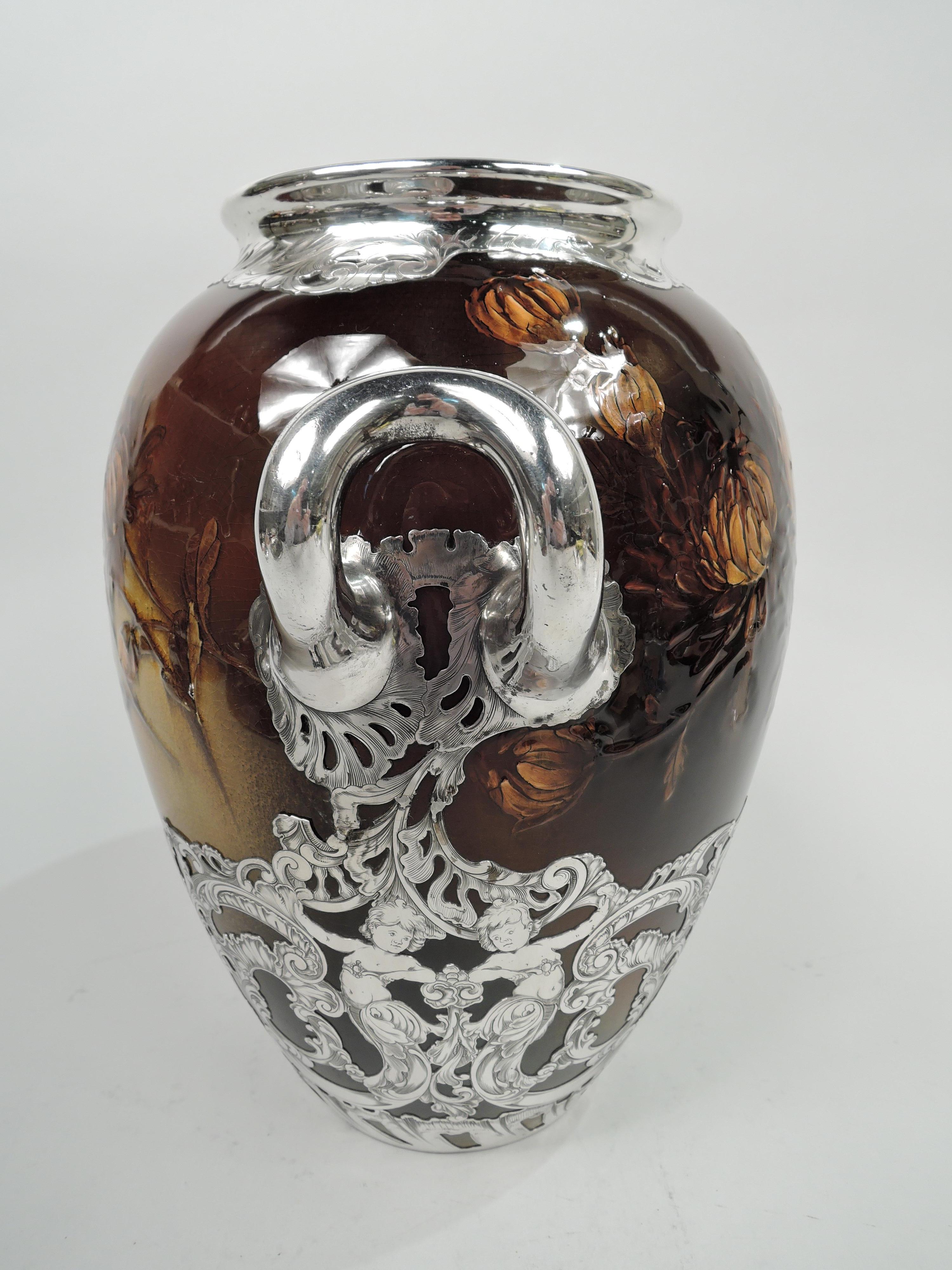 Large Art Nouveau Craftsman glazed earthenware vase. Made by Rookwood Pottery in Cincinnati in 1892. Ovoid with silver bracket handles. Shaded orange chrysanthemums emerging from umbrous brown ground. Overlay in form of dense leafing scrollwork and