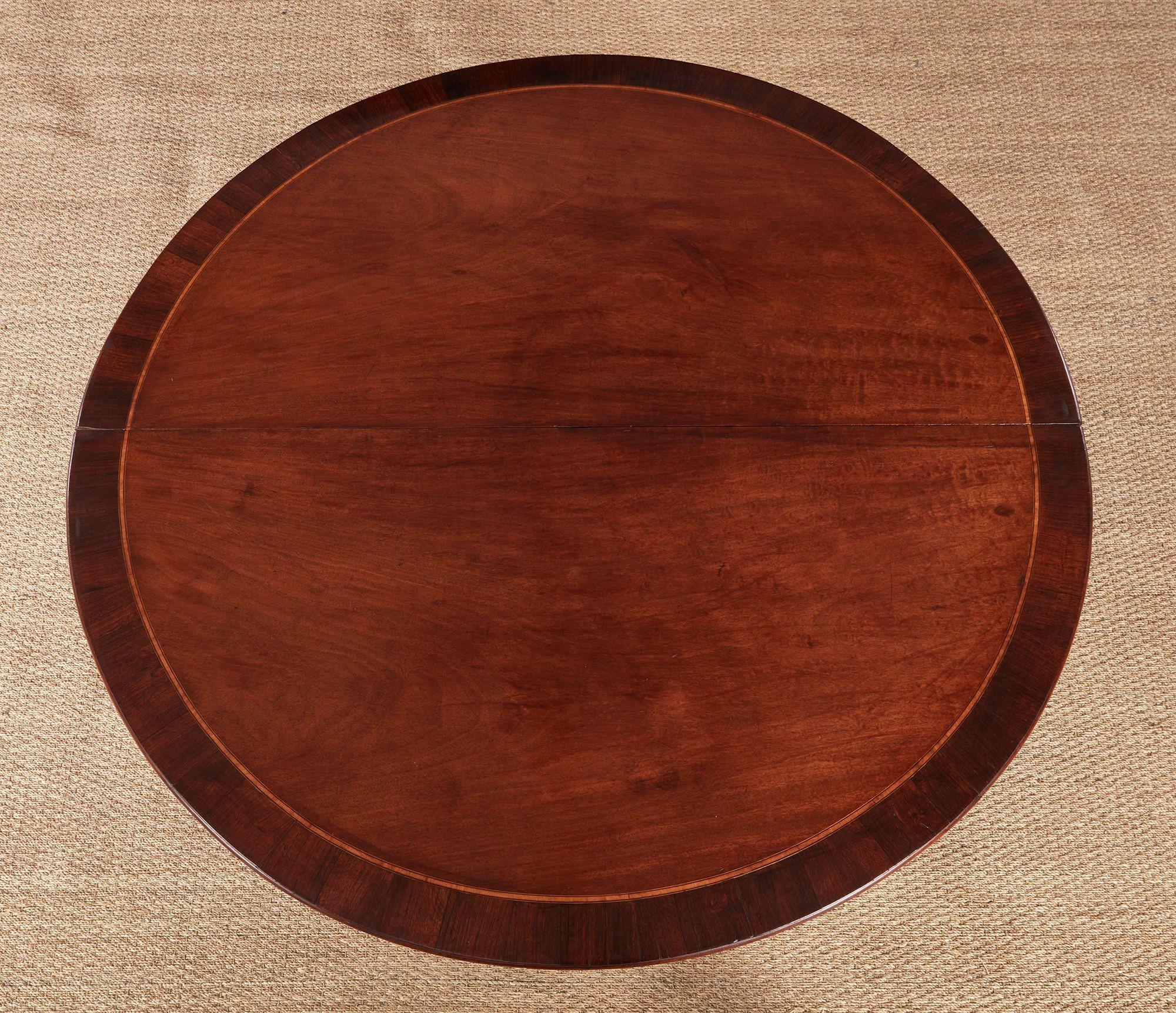 An 18th century five-foot diameter round dining table in wonderfully figured solid mahogany with rosewood banding, composed of two demilune bookmatched halves, each with a thin apron above four tapering square section legs ending in spade feet.  Can