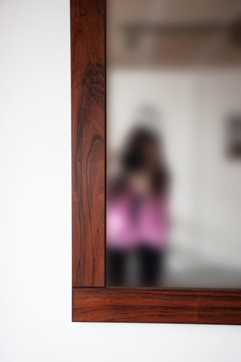 A large wall mirror with a wide, minimalist frame in richly grained rosewood.