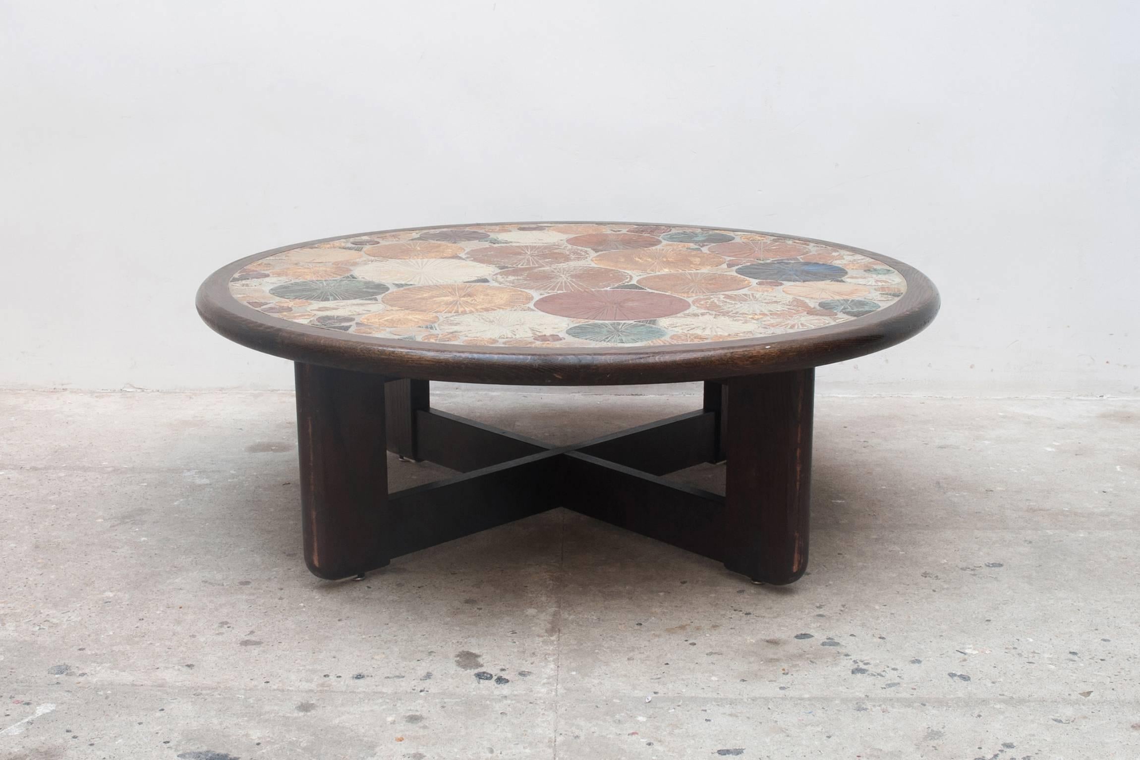 Large round ceramic coffee table was designed by Tue Poulsen in 1963, and was manufactured in Denmark by Haslev Møbelsnedkeri. The table has a dark stained oak wooden edge and cross feet, features multiple colored blue, green brown, grey, white and