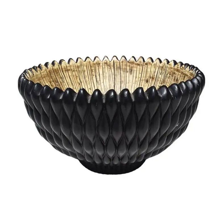 A large black textured decorative bowl in black with a brown incised interior. This bowl has a textured knobby exterior in black. The interior is in cream, with brown and black scored lines. Use this as a fruit bowl on a table or counter in a