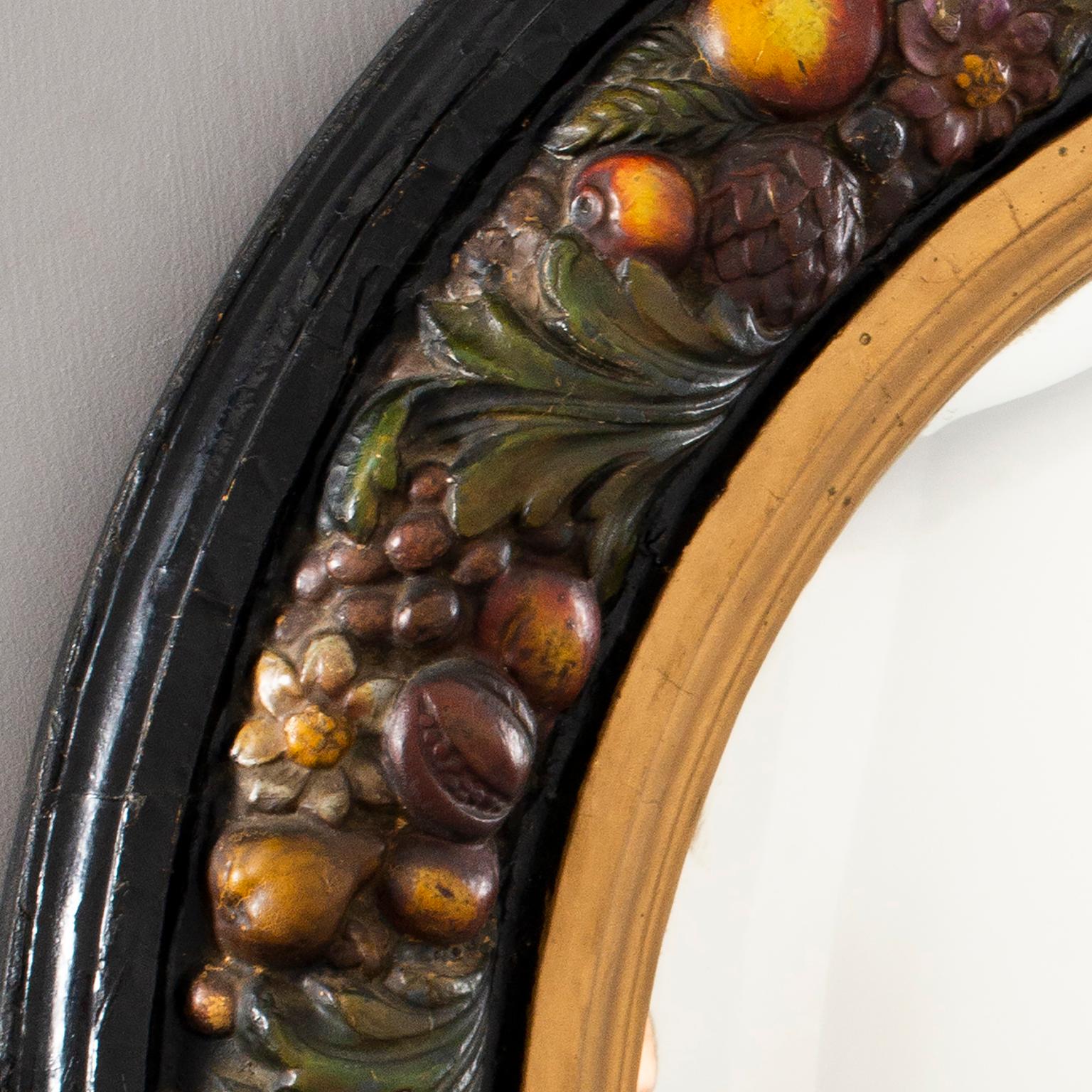Large round French mirror has a traditional Barbola style frame of fruit and flowers on a black background with gilded inner rim, circa 1930s.