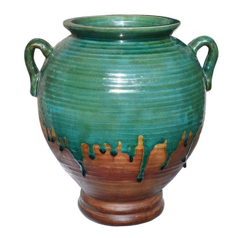 A large round brown ceramic planter with a gorgeous verdigris green drip glaze. Perfect for a patio or foyer, this unusual vessel features two round applied handles on each side and is covered in a vibrant green. The blue-green glaze starts at the