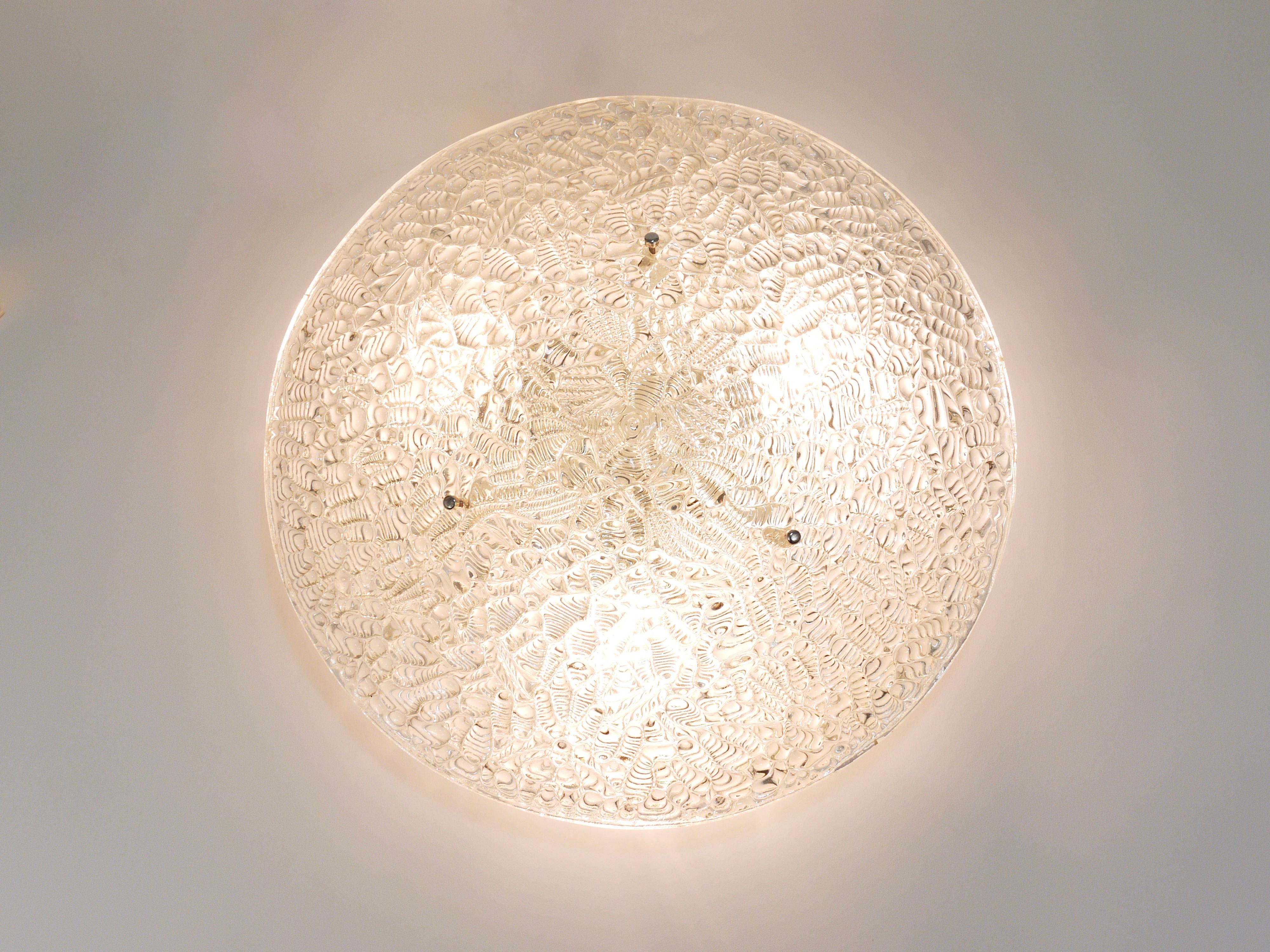 A beautiful and elegant modernist flush mount / ceiling lamp from the 1960s by J.T. Kalmar, Austria. A charming light fixture, it has a domed 18 in diameter lampshade, made of solid textured melting ice glass on a white metal base with three tiny