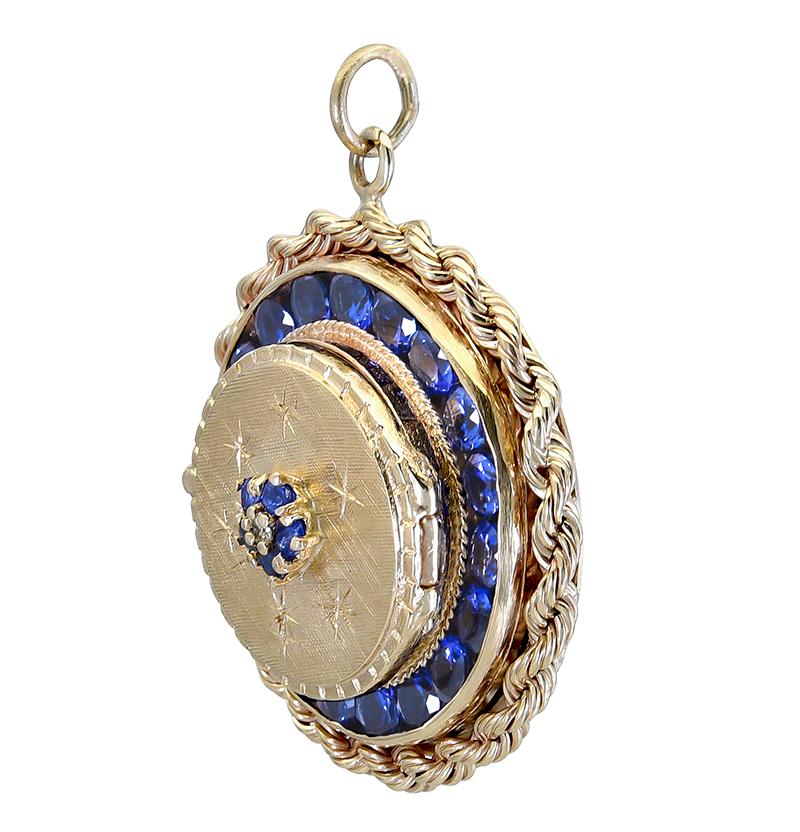 Extra-large and well-detailed round locket.  Central design of five round sapphires and a diamond, surrounded by six diamonds in starburst pattern with textured gold.  Bordered by shiny gold engraved detail with hinge on edge opens to hold space for